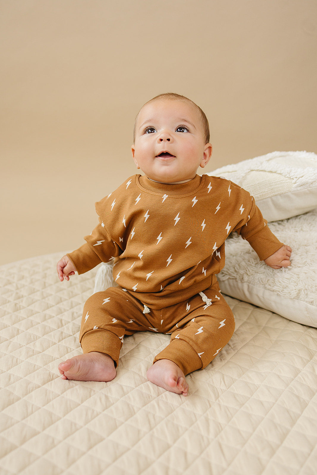 Fall Bolts Kids Lounge Set featuring a baby in a lightning bolt printed brown outfit sitting on a beige quilt.