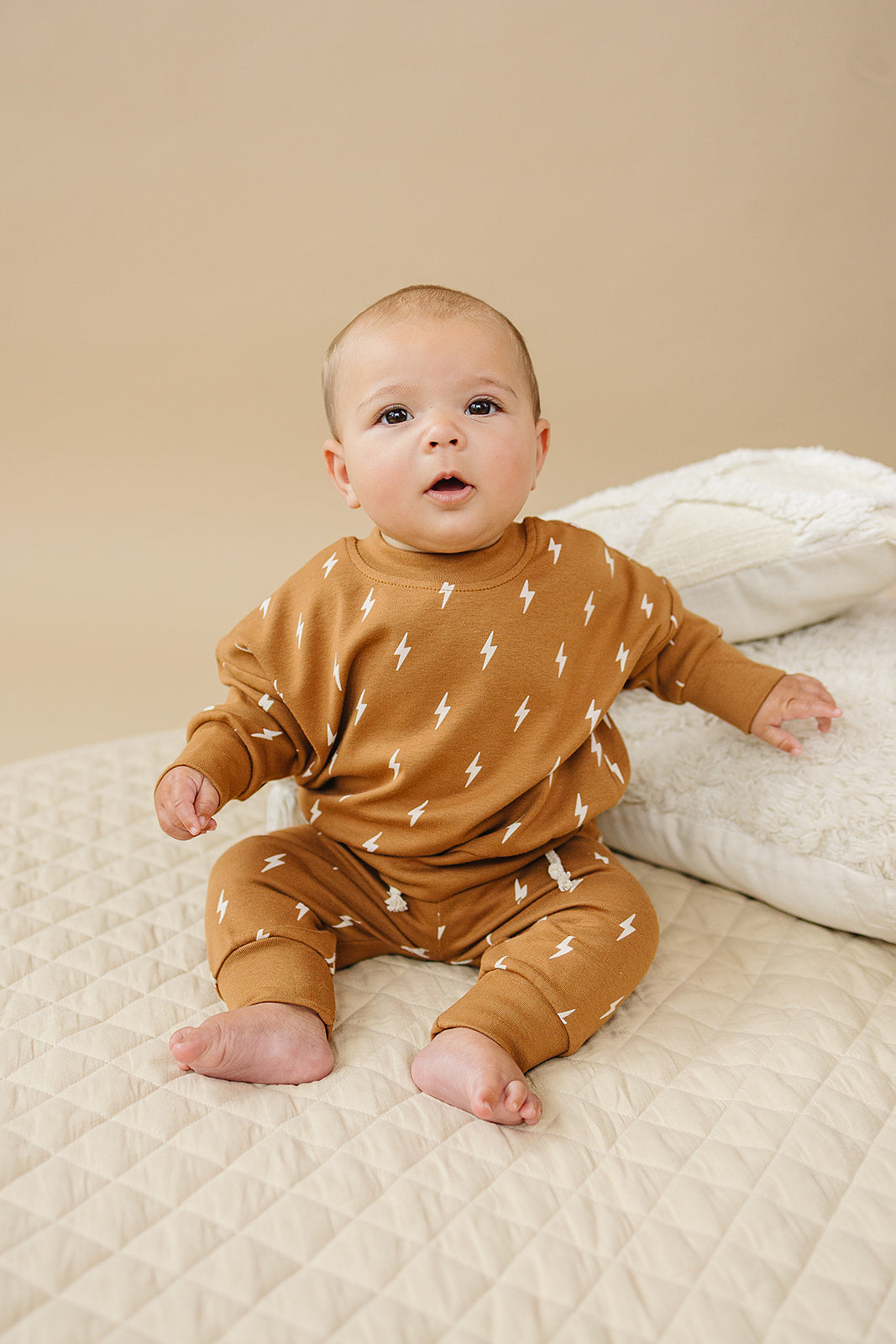 Cute baby wearing the Fall Bolts Kids Lounge Set with a lightning bolt print, sitting on a quilted blanket.