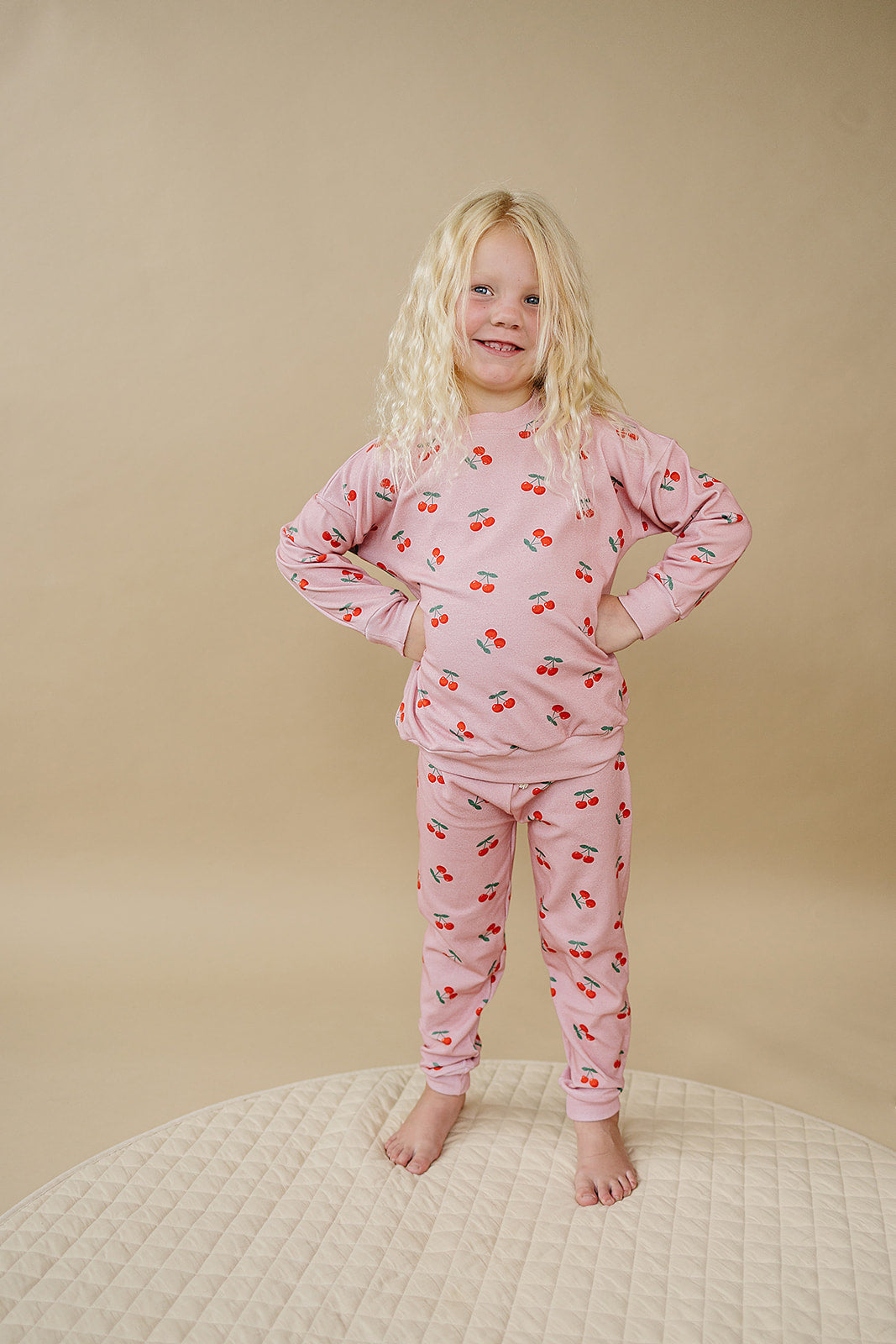 Blush Cherry Kids Lounge Set worn by a girl with curly hair, featuring a pink cherry-print top and jogger bottoms.