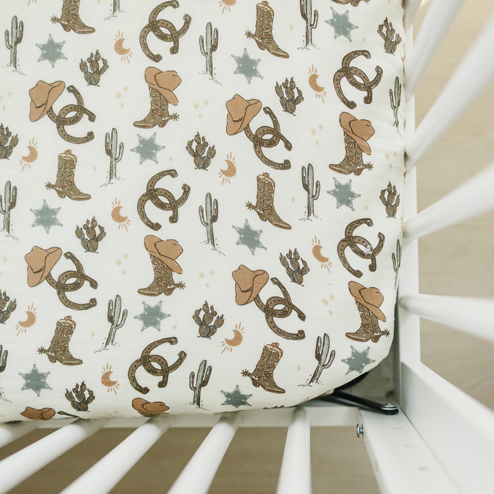 Muslin crib sheet featuring outlaw cowboy design with boots, hats, cacti, and stars for a playful nursery decor.