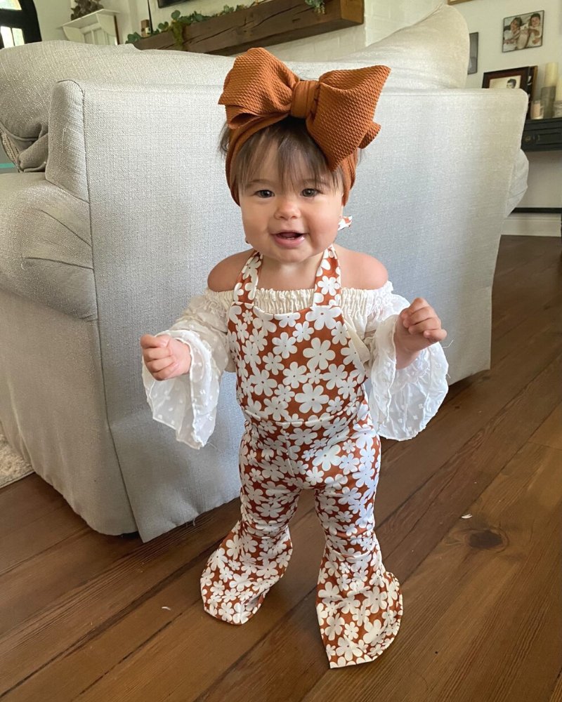 Toddler wearing Andi pleated bell bottom jumpsuit with floral print and a large bow, showcasing a playful bohemian style.