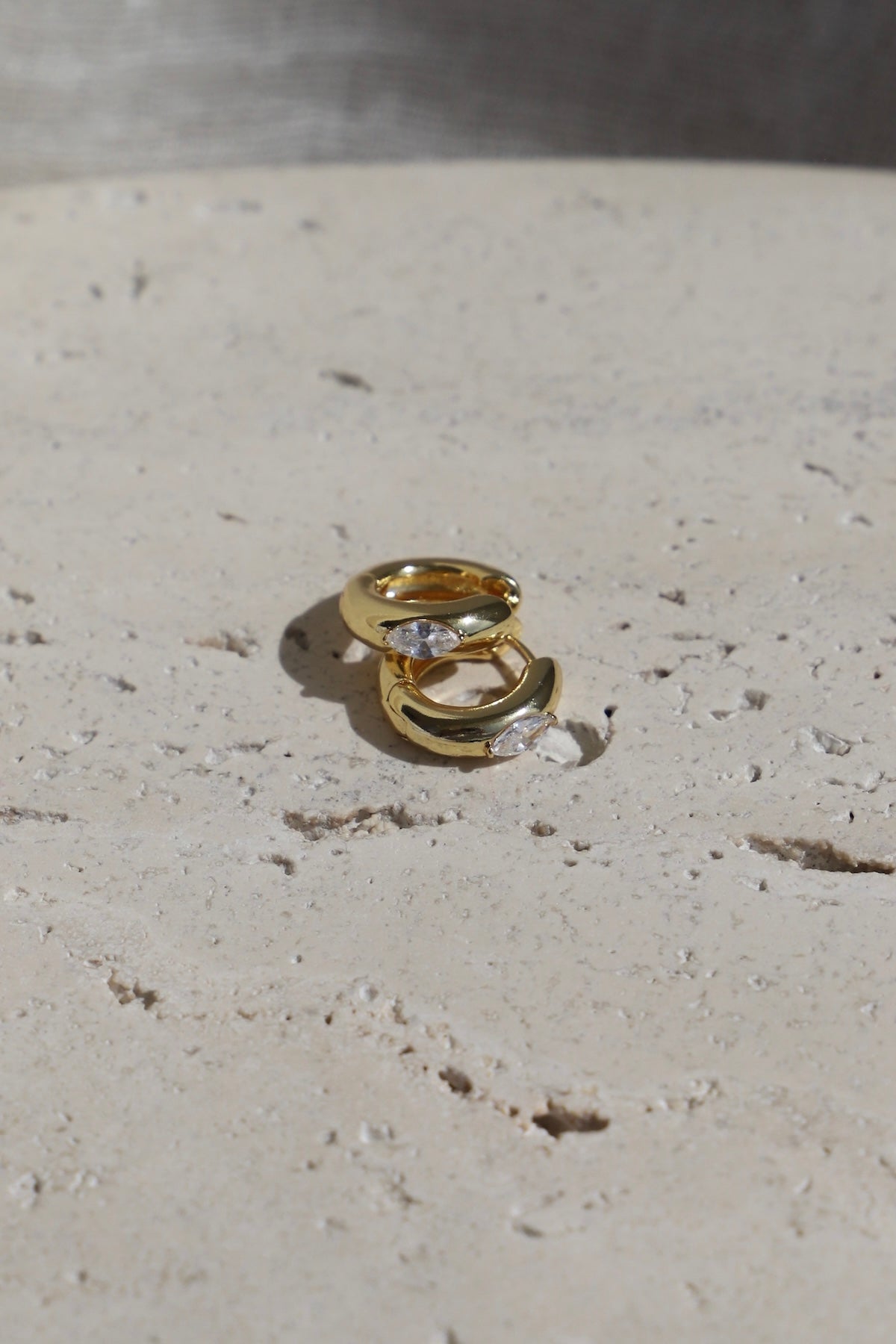 Aurum Hoops gold-toned earrings on a textured stone surface, showcasing a chic and lightweight design.