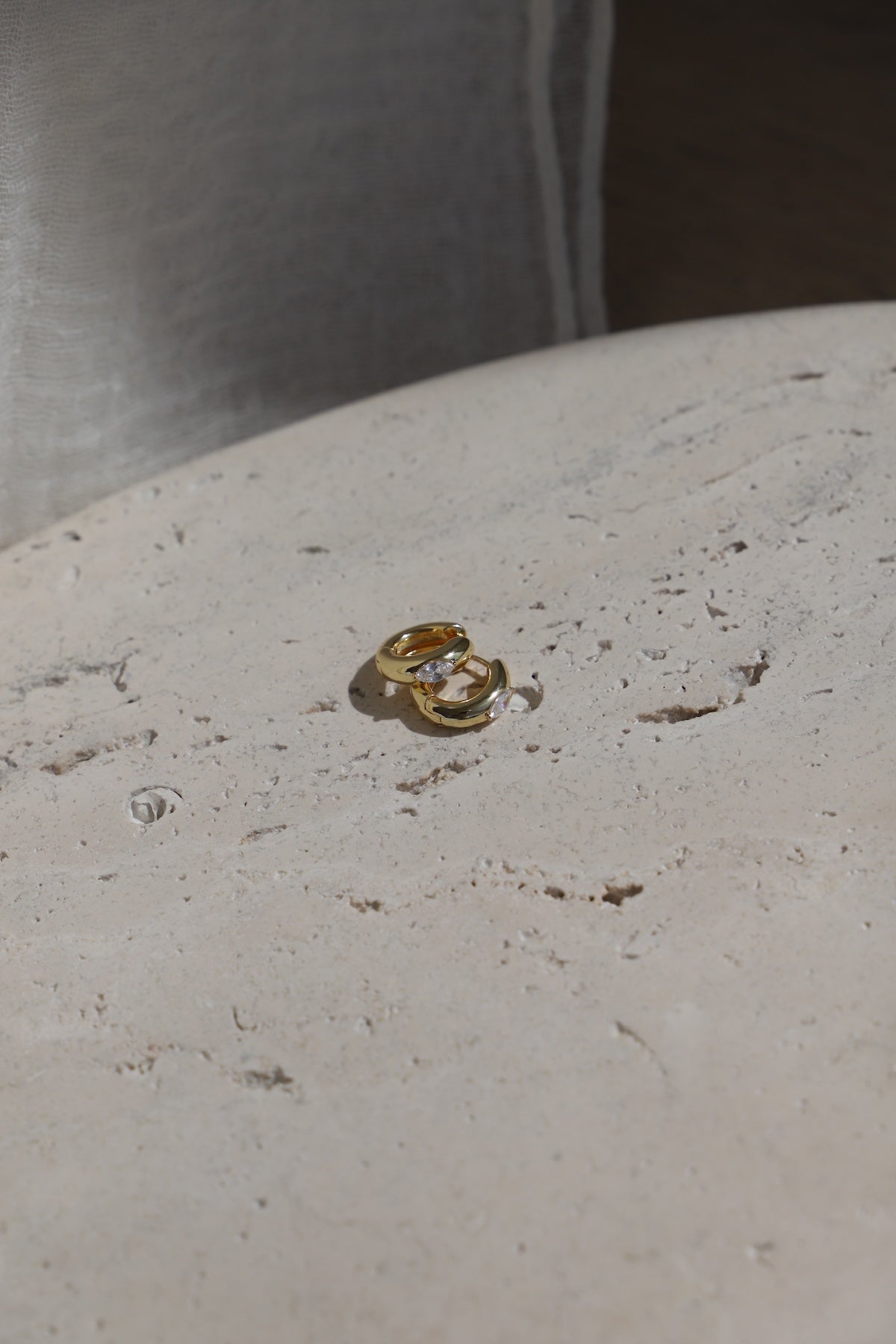 Aurum Hoops gold-toned earrings resting on a textured stone surface, showcasing a chic and minimalist design.