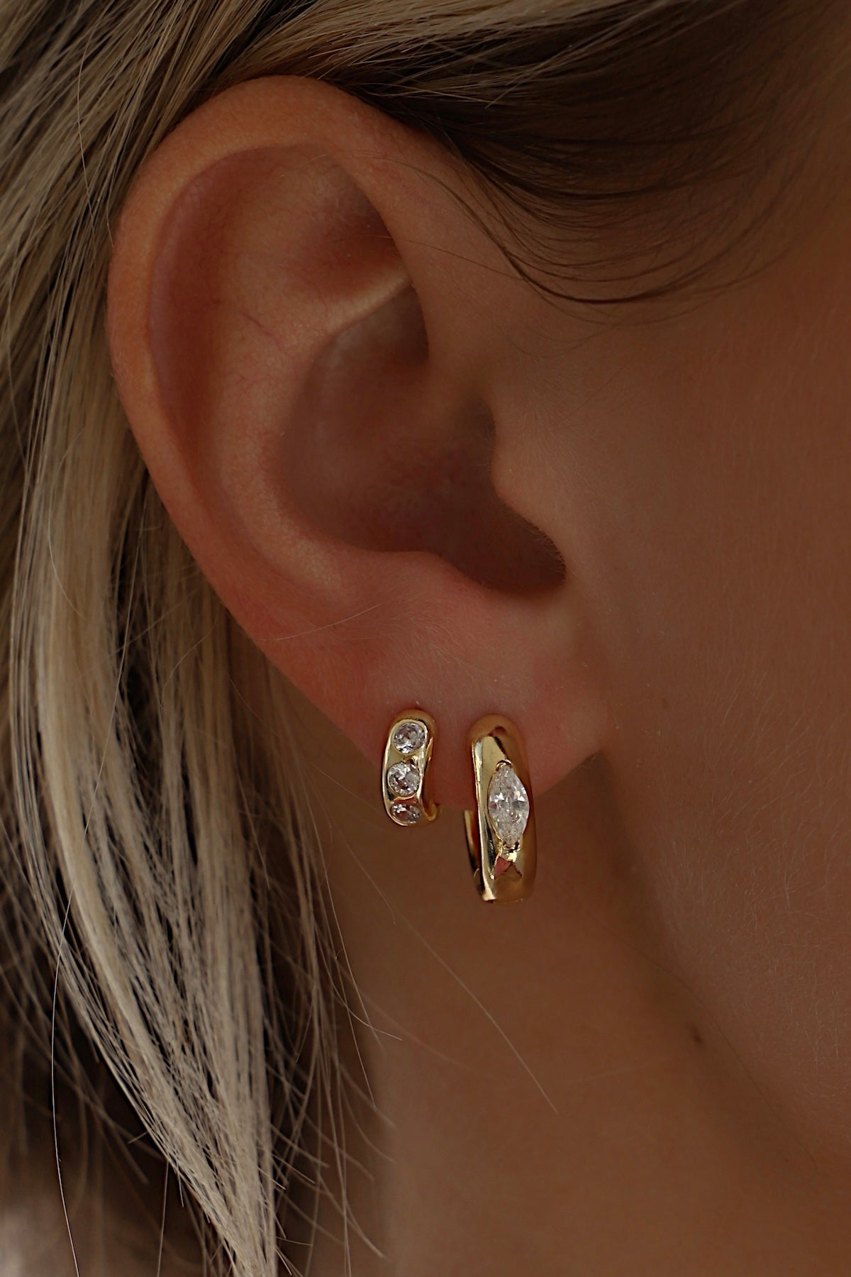Close-up of Aurum Hoops gold-toned earrings worn in a model's ear, showcasing a chic and minimal design.