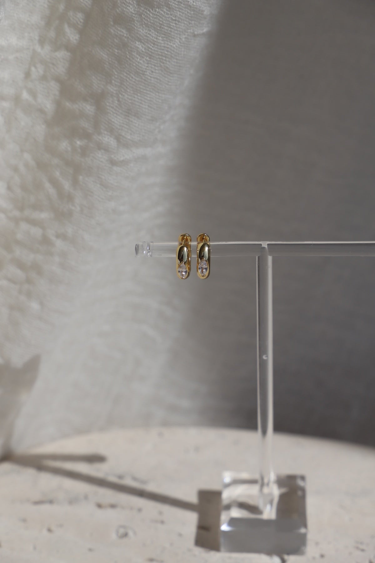 Aurum Hoops gold-toned earrings displayed on a clear stand, highlighting their lightweight and chic design.