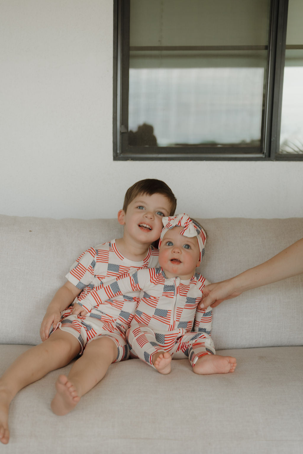 Two children wearing patriotic bamboo short set with Americana print, sitting on a couch in a cozy indoor setting.