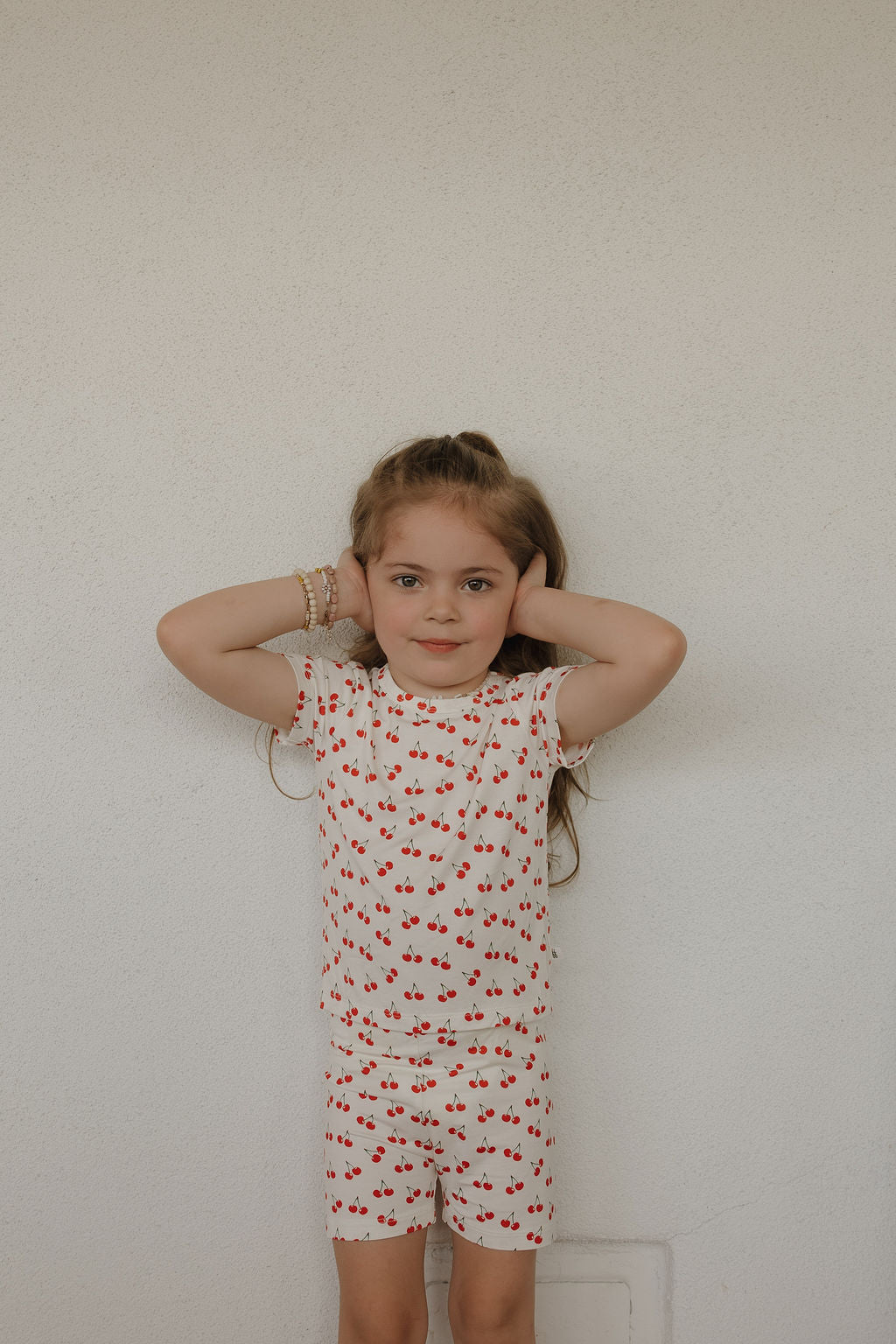 Child wearing bamboo short set with sweetheart cherry print on blush pink background.