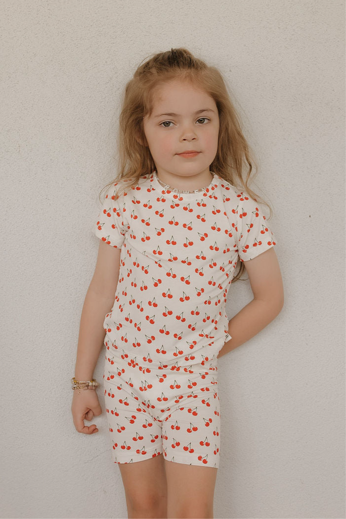 Child wearing a bamboo short set with a playful cherry print on a blush pink background.