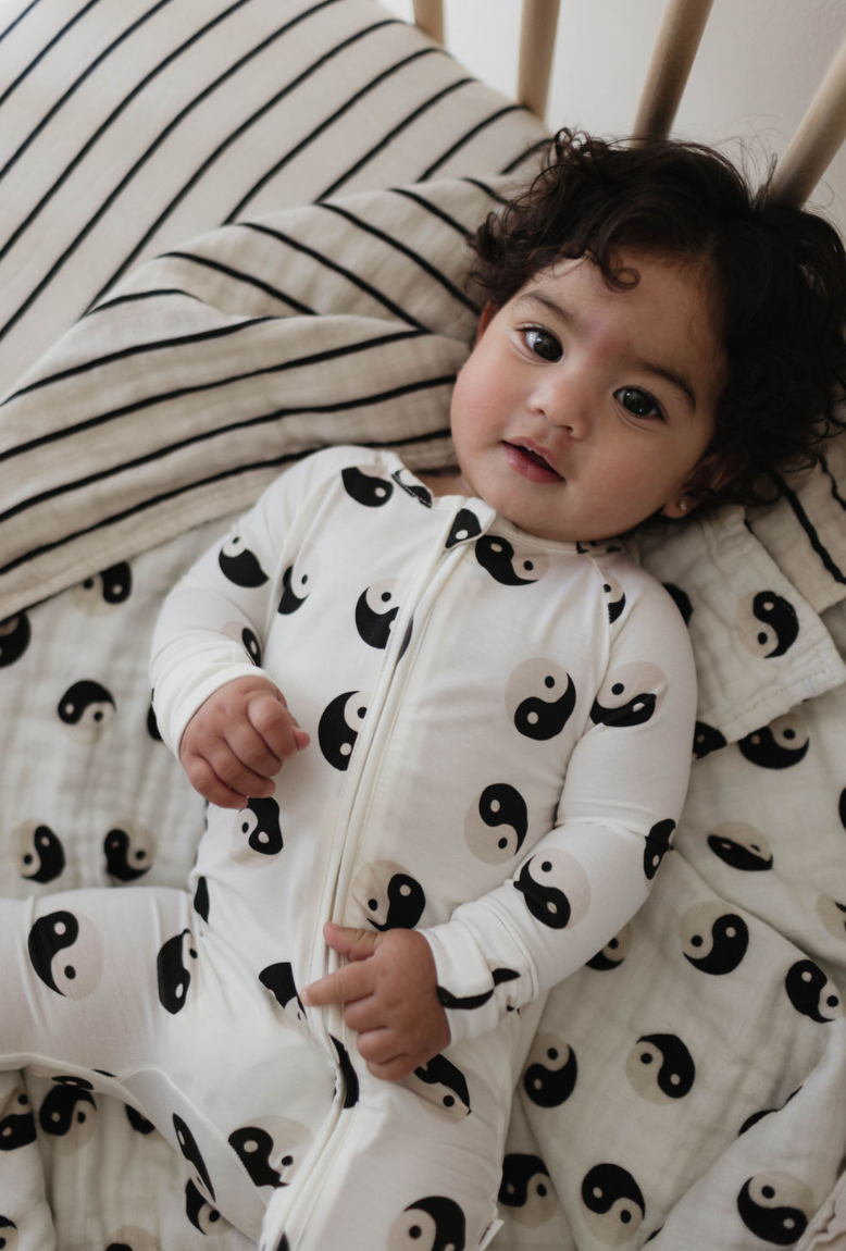 Baby in black and white yin yang bamboo zip pajamas, resting on a cozy striped blanket.