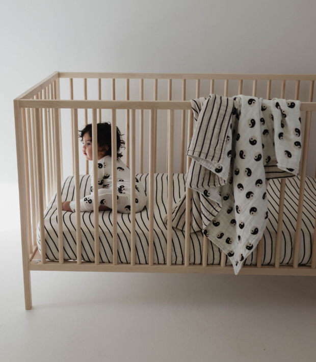Baby in bamboo zip pajamas in a crib, with a cozy blanket, featuring a black and white yin yang design.