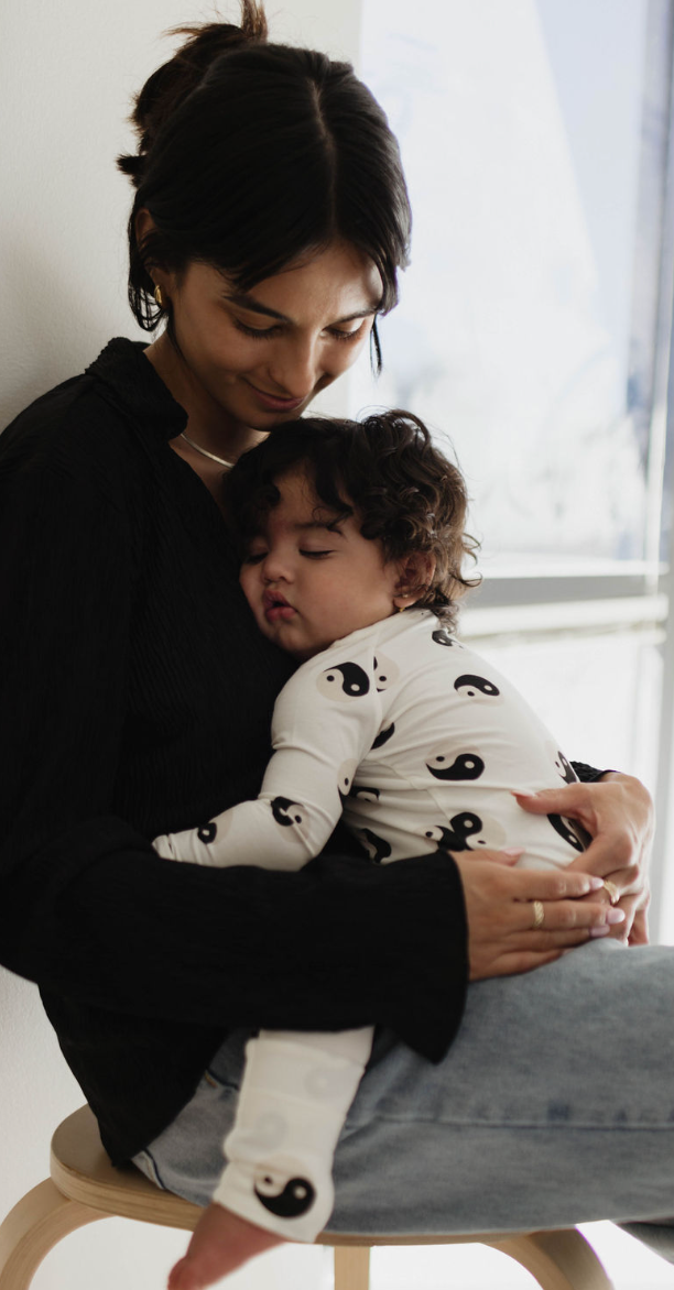 Mother holding a sleeping toddler in cozy black and white yin yang bamboo zip pajamas.