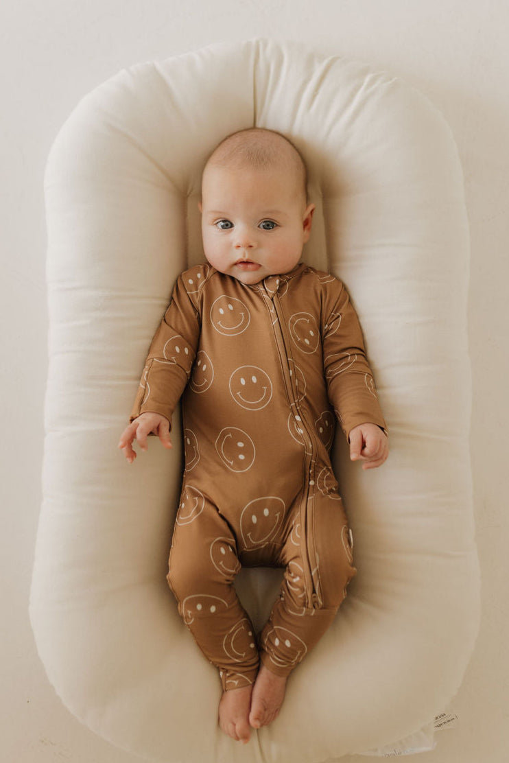 Happy baby in bamboo zip pajamas with smiley faces, lying on a cozy surface.