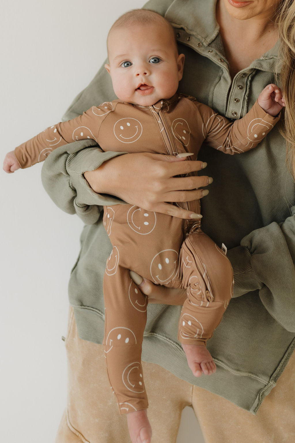 Baby wearing soft bamboo zip pajamas with smiley face print, held by caregiver in cozy outfit.