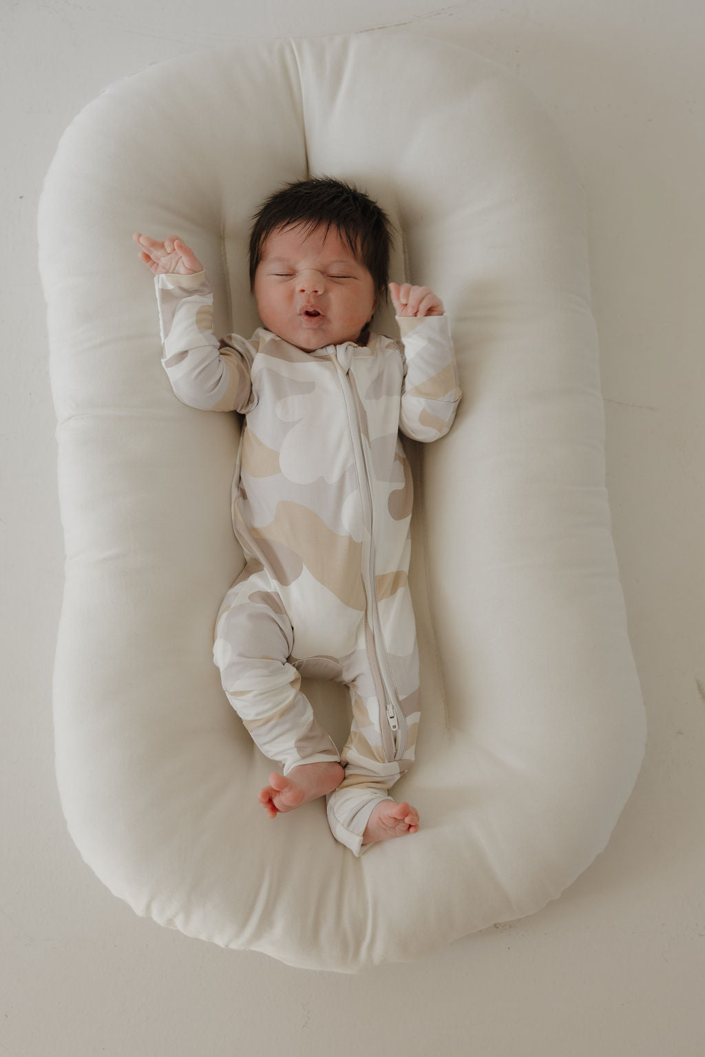 Baby sleeping peacefully in bamboo zip pajamas with a modern camo design.