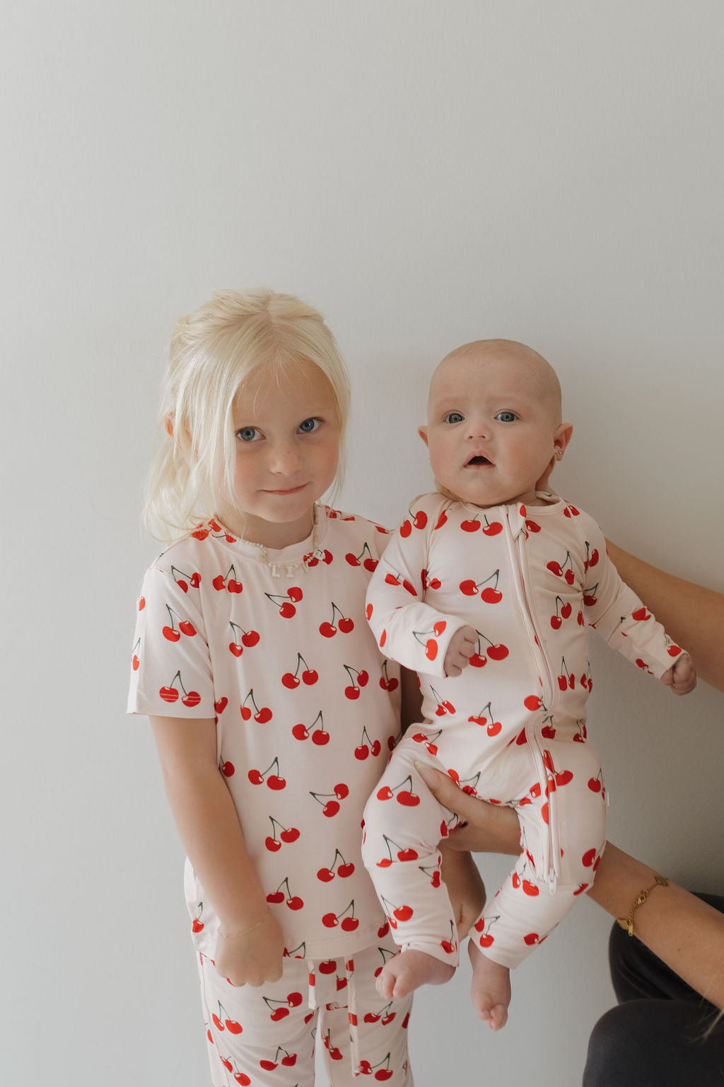 Two children wearing Cherry Orchard bamboo zip pajamas with a cherry print, perfect for cozy nap and bedtime.