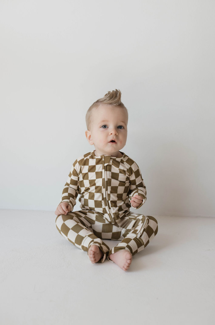 Baby in olive checkerboard bamboo zip pajamas, featuring a comfortable design and playful pattern.
