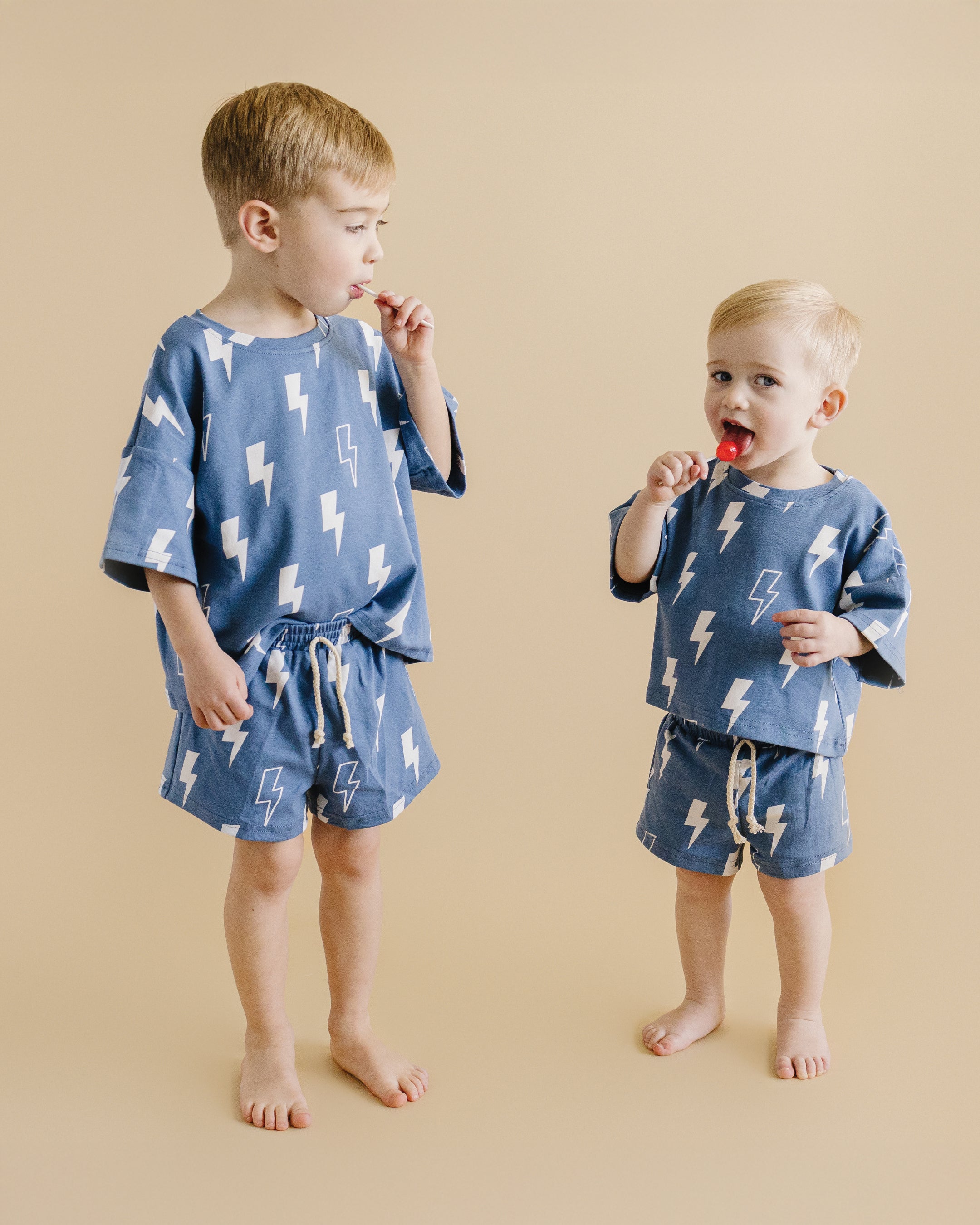 Two kids wearing a playful blue bolt shorts set, featuring an oversized tee and matching shorts, on a neutral background.