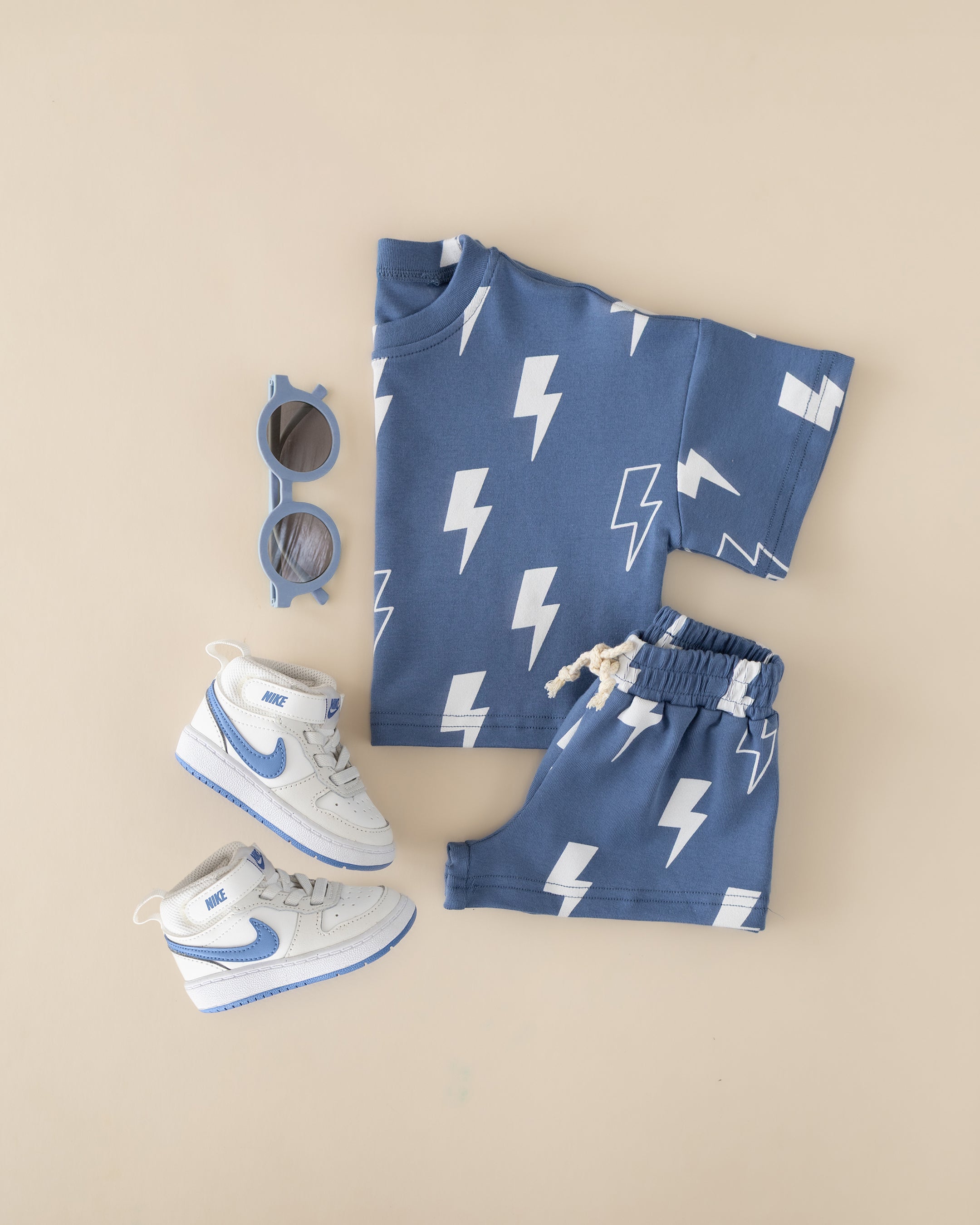 Blue shorts set with lightning bolt print, matching shorts, sunglasses, and sneakers for stylish kids.