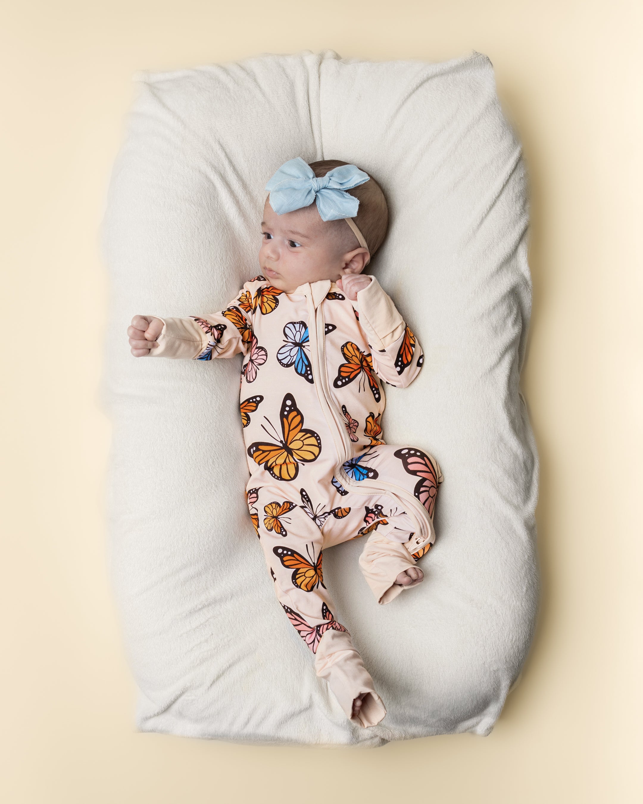 Baby wearing a pastel butterfly print bamboo zip romper on a soft cushion, showcasing comfort and style.