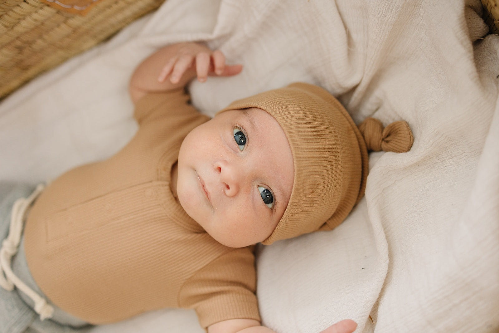 Baby in a beige outfit and hat lying on a soft surface