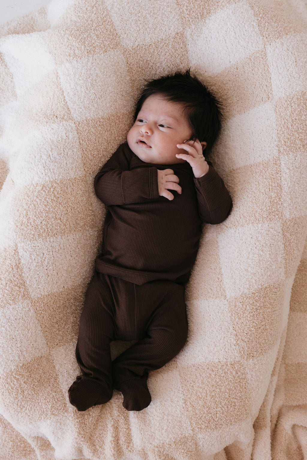 Baby wearing cozy bamboo pajamas in neutral brown color, resting on a soft blanket, perfect for bedtime.