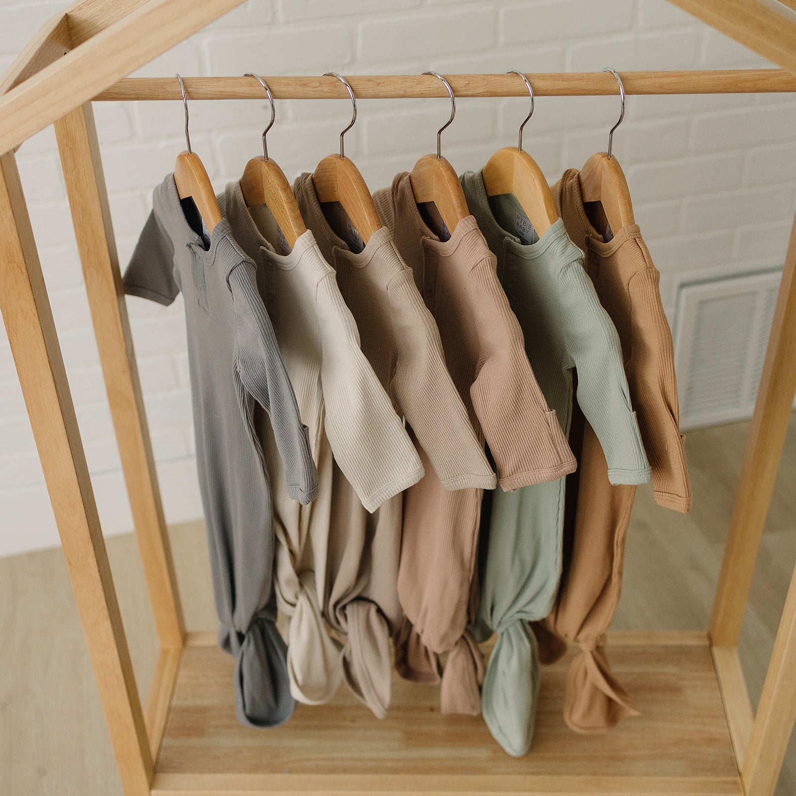 Collection of organic cotton ribbed knot gowns in neutral tones hanging on wood display, ideal for newborns.