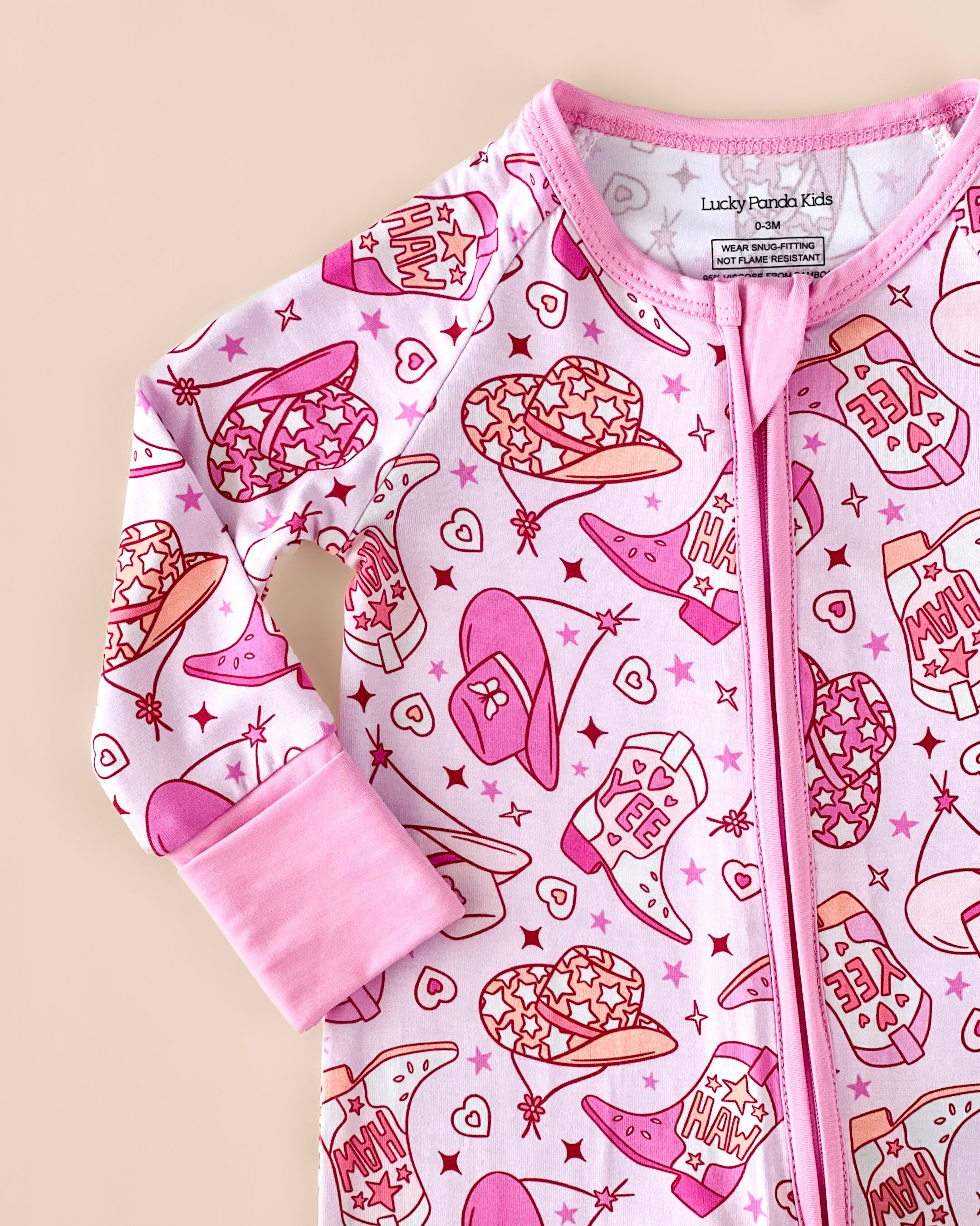 Bamboo zip romper in playful pink cowgirl print featuring boots and hats, perfect for cozy baby nights.