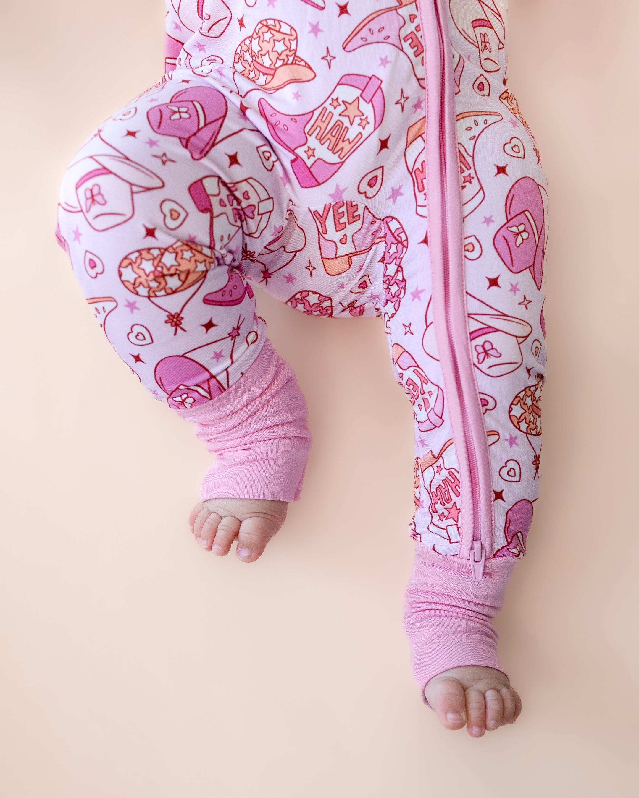 Bamboo zip romper for babies featuring playful cowgirl print with boots and hats, designed for comfort and easy changes.
