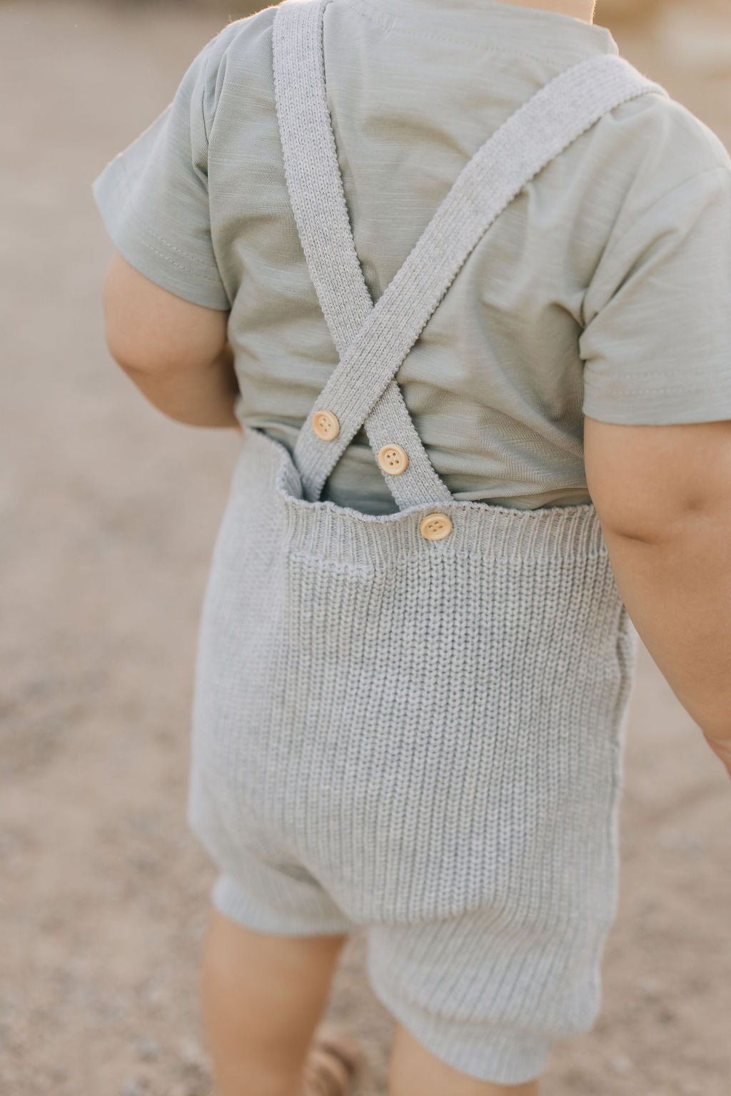 Baby in heather grey knit overalls with button straps, showcasing a cozy, casual style for toddlers.