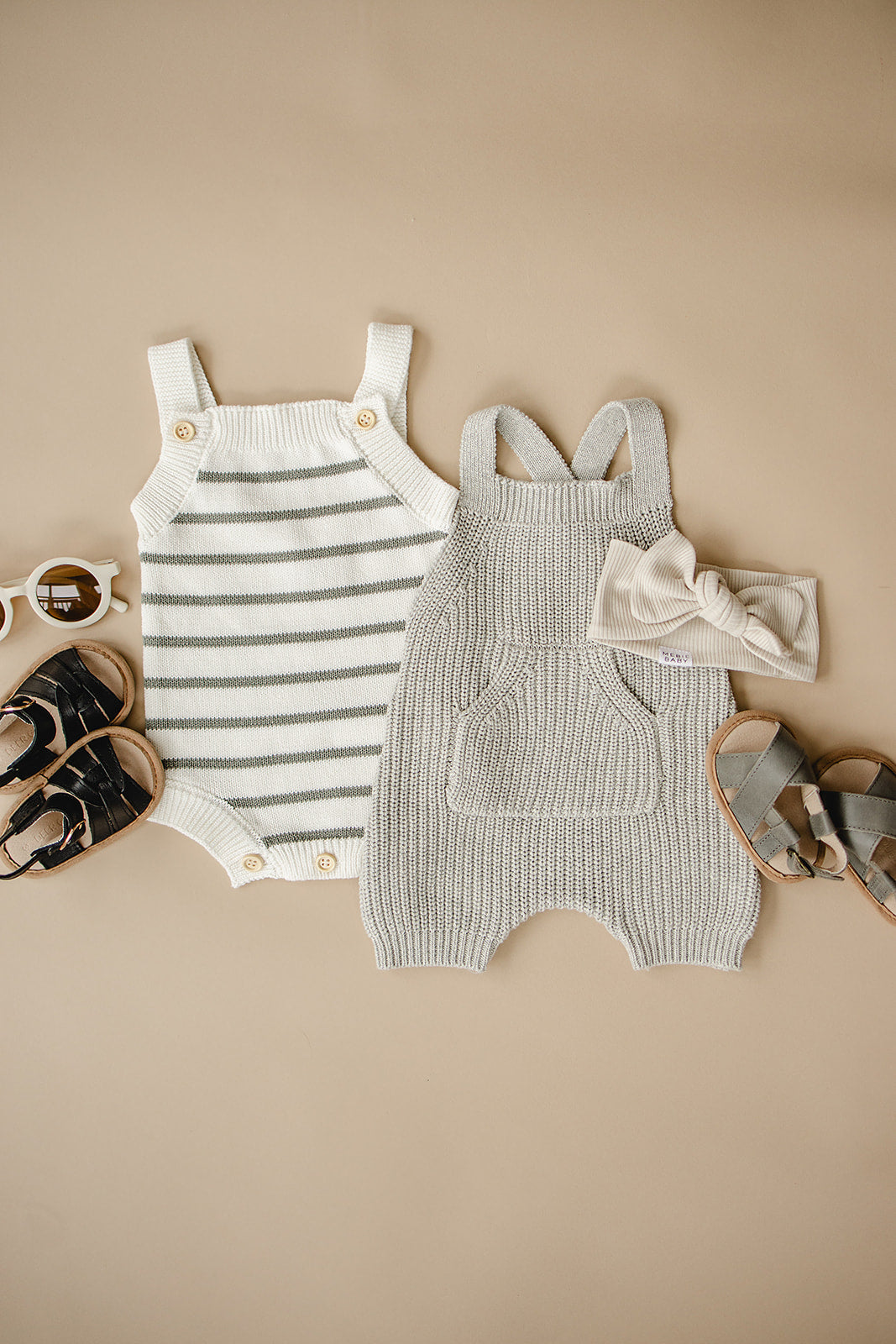Two cozy knit overalls in heather grey and striped design, paired with baby accessories on a beige background.
