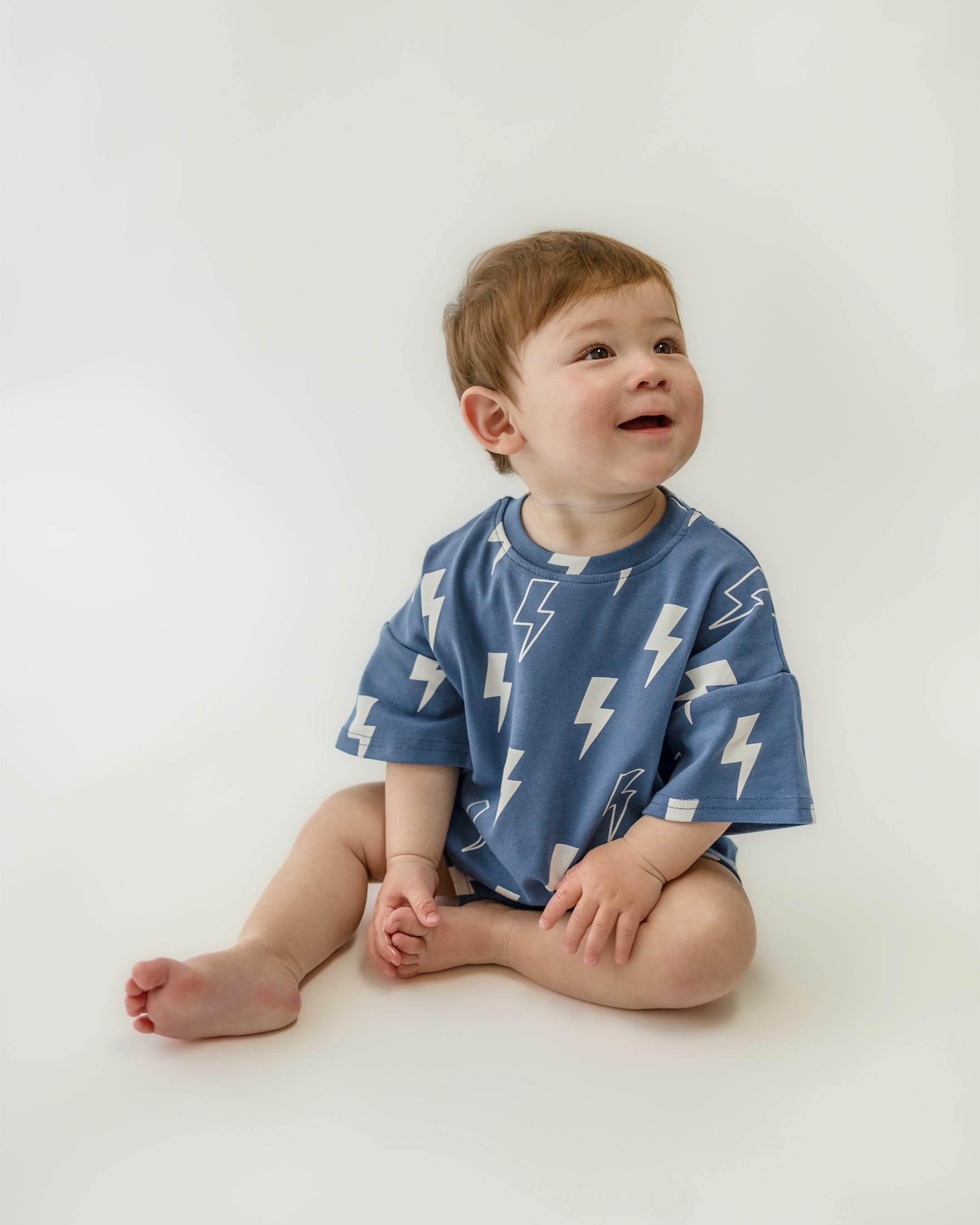 Cute child in oversized blue bolt print tee, sitting and smiling, showcasing playful fashion for kids.