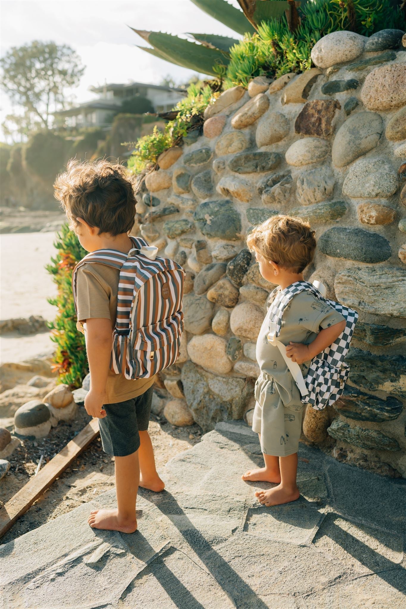 Two kids in playful mini backpacks by the beach, showcasing vibrant styles for fun outdoor adventures.