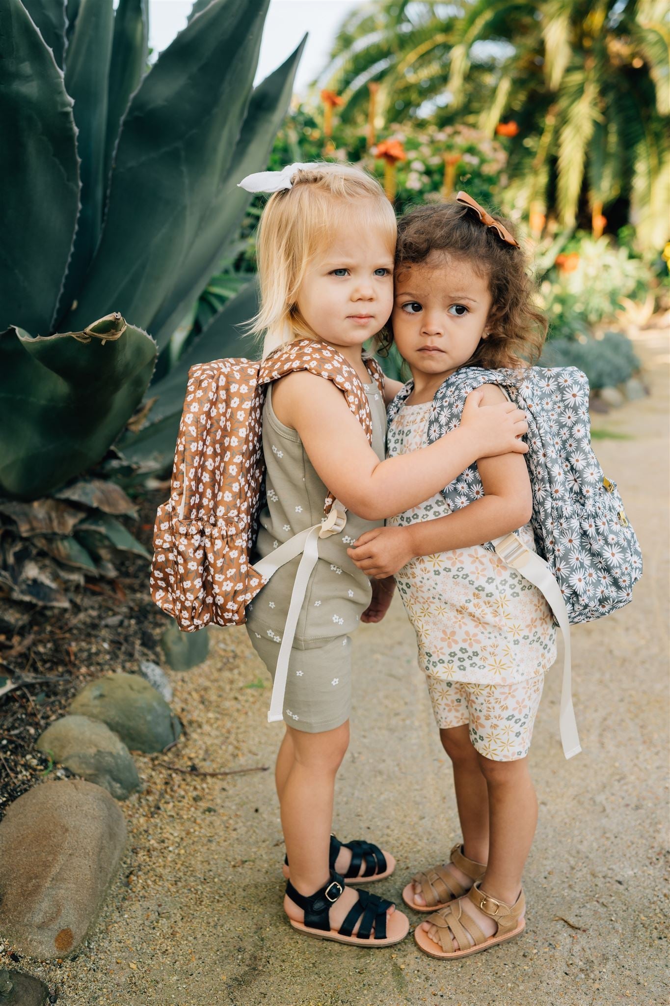 Two children wearing floral mini backpacks in a lush outdoor setting, perfect for kids on the go.