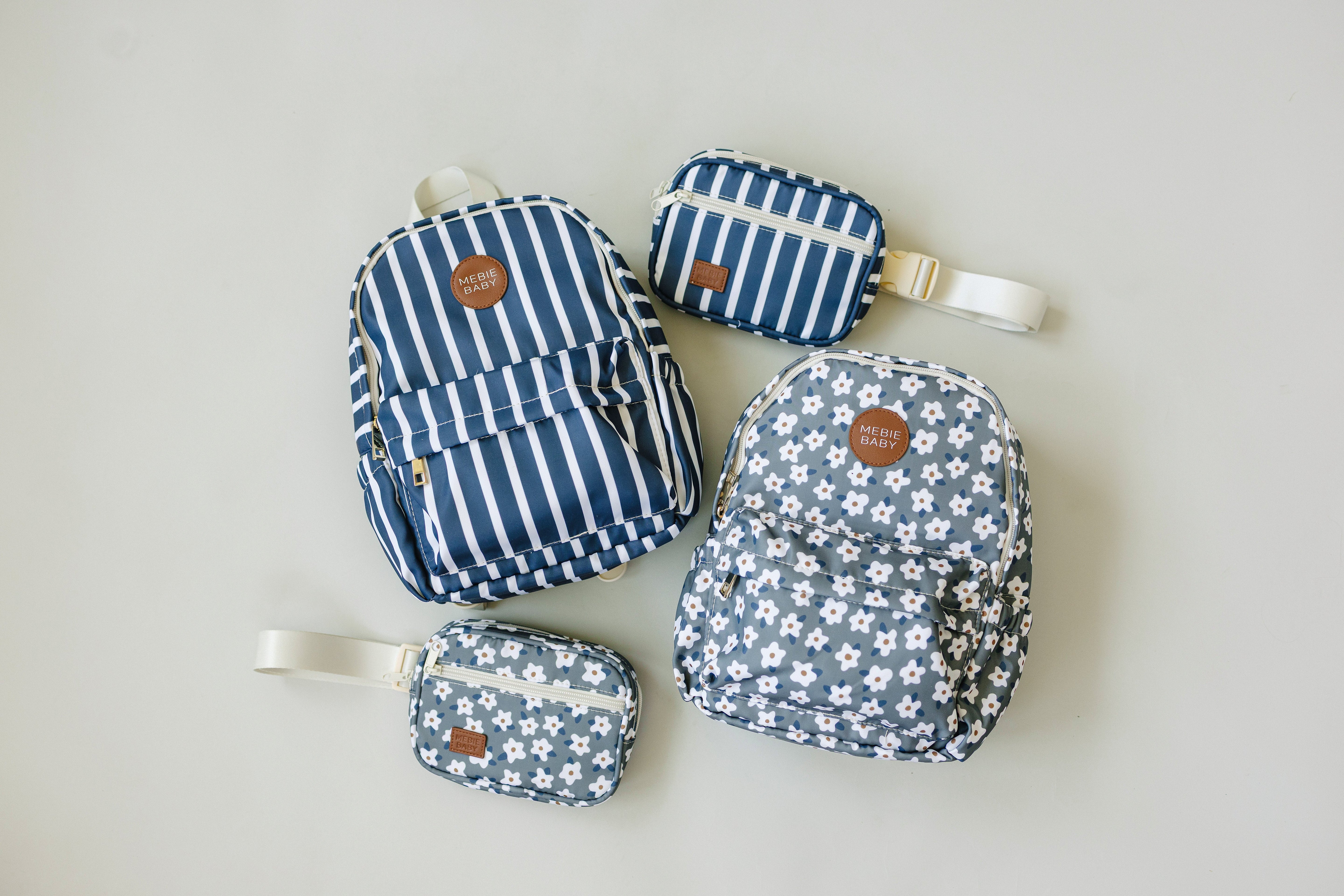 Collection of navy striped and floral backpacks and mini bags on a neutral background.
