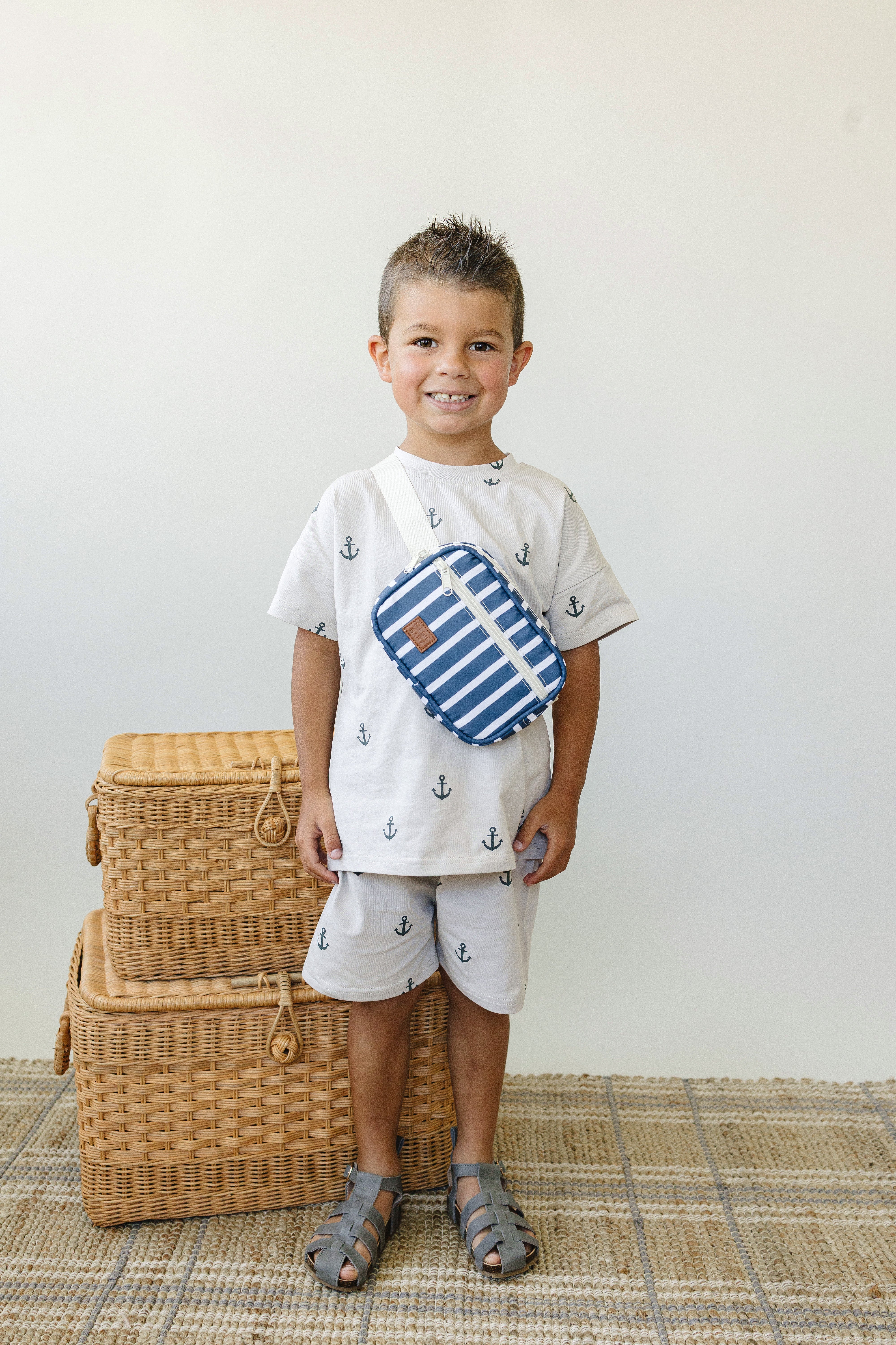 Smiling boy wearing a navy stripe mini fanny pack, styled with anchor-patterned shirt and shorts.