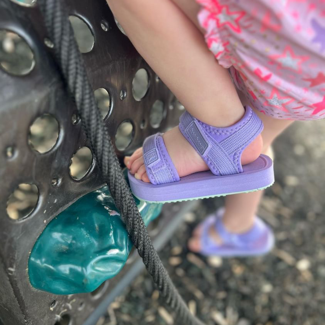 Toddler wearing purple Ned Sandal Water Shoes climbing a playground structure, showcasing comfort and flexibility.