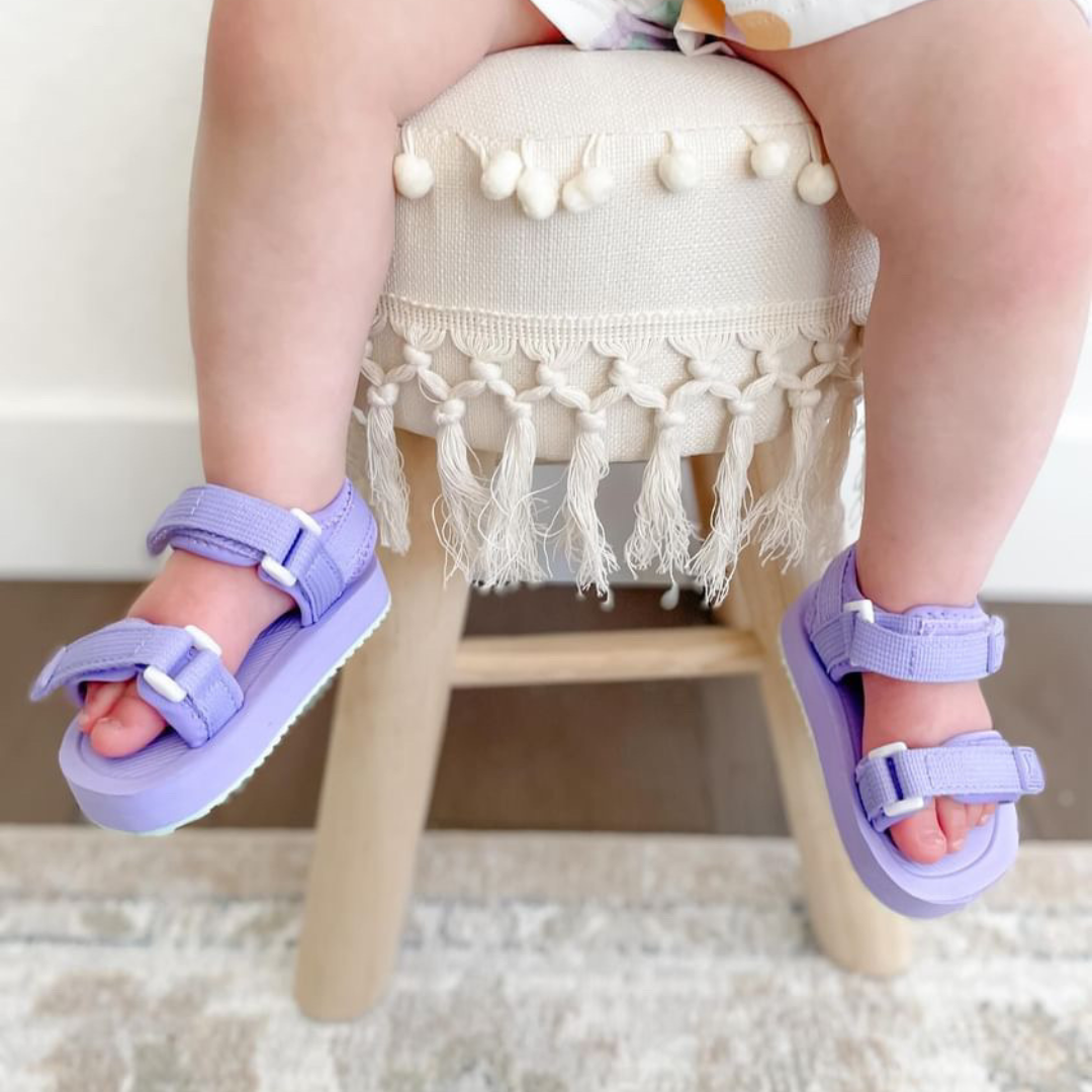 Toddler wearing purple Ned Sandal Water Shoes on a decorative stool, perfect for summer adventures.