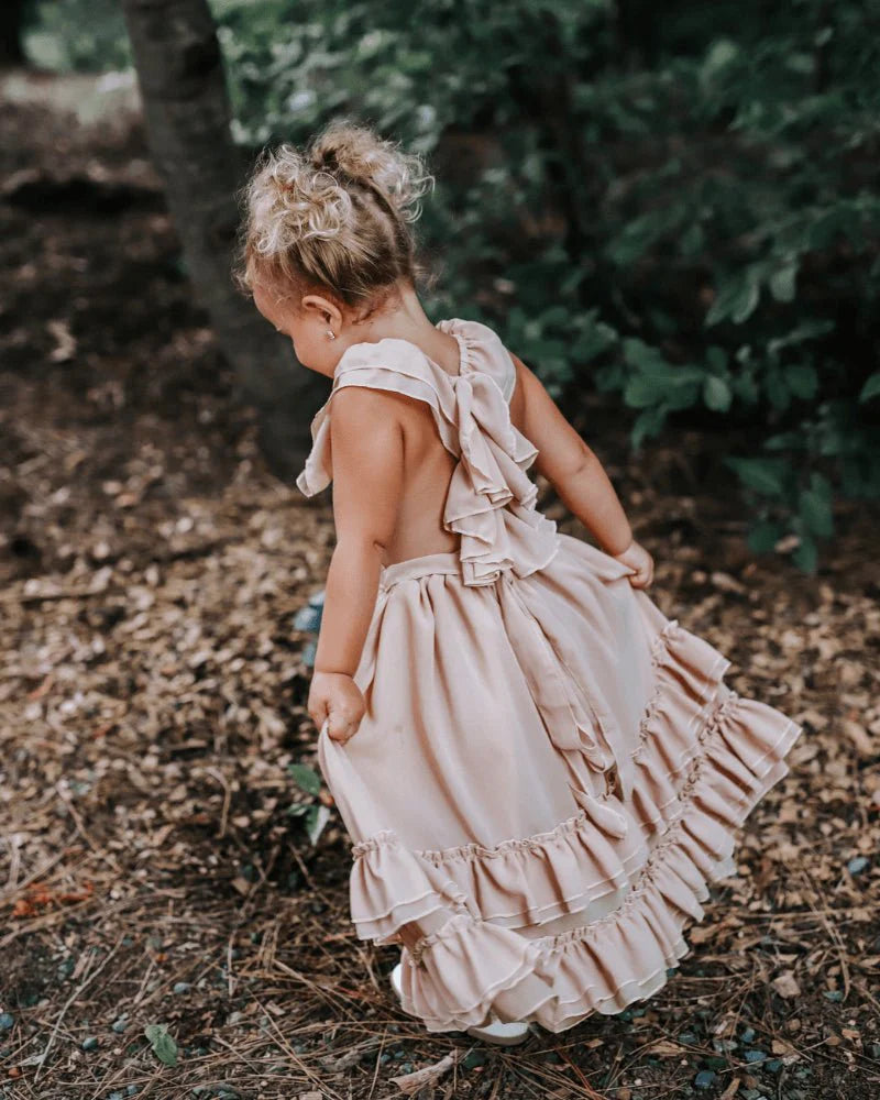 Little girl wearing a champagne dress with ruffles, showcasing a playful twirl in nature.