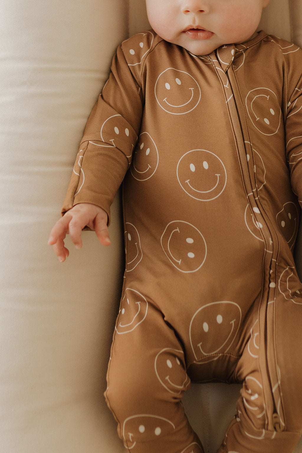 Baby wearing soft bamboo zip pajamas with smiley face print in sandstone color.