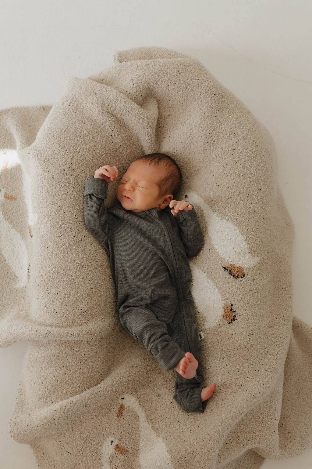 Newborn baby wearing shadow bamboo zip pajamas, lying on a cozy blanket with a minimalist design.