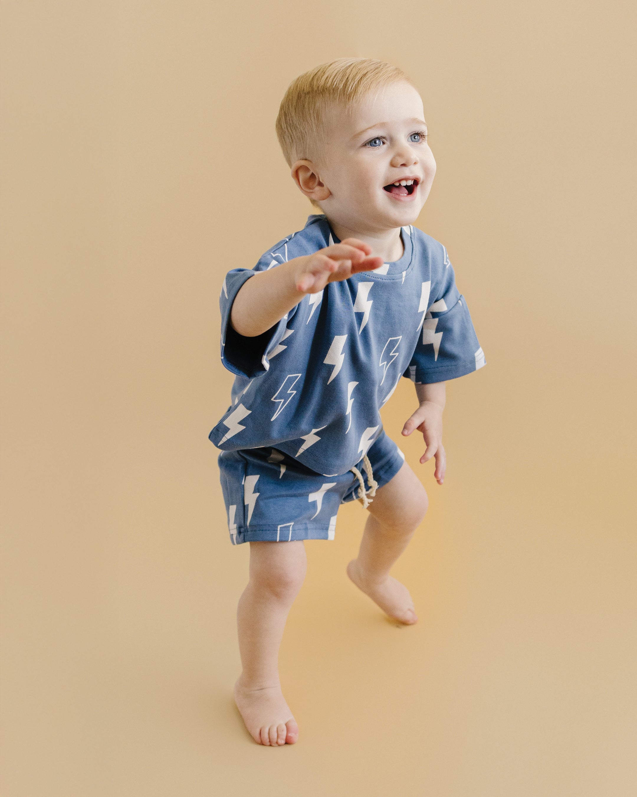 Cute child wearing a blue bolts shorts set, smiling and playing, showcasing the relaxed-fit tee and elastic-waist shorts.