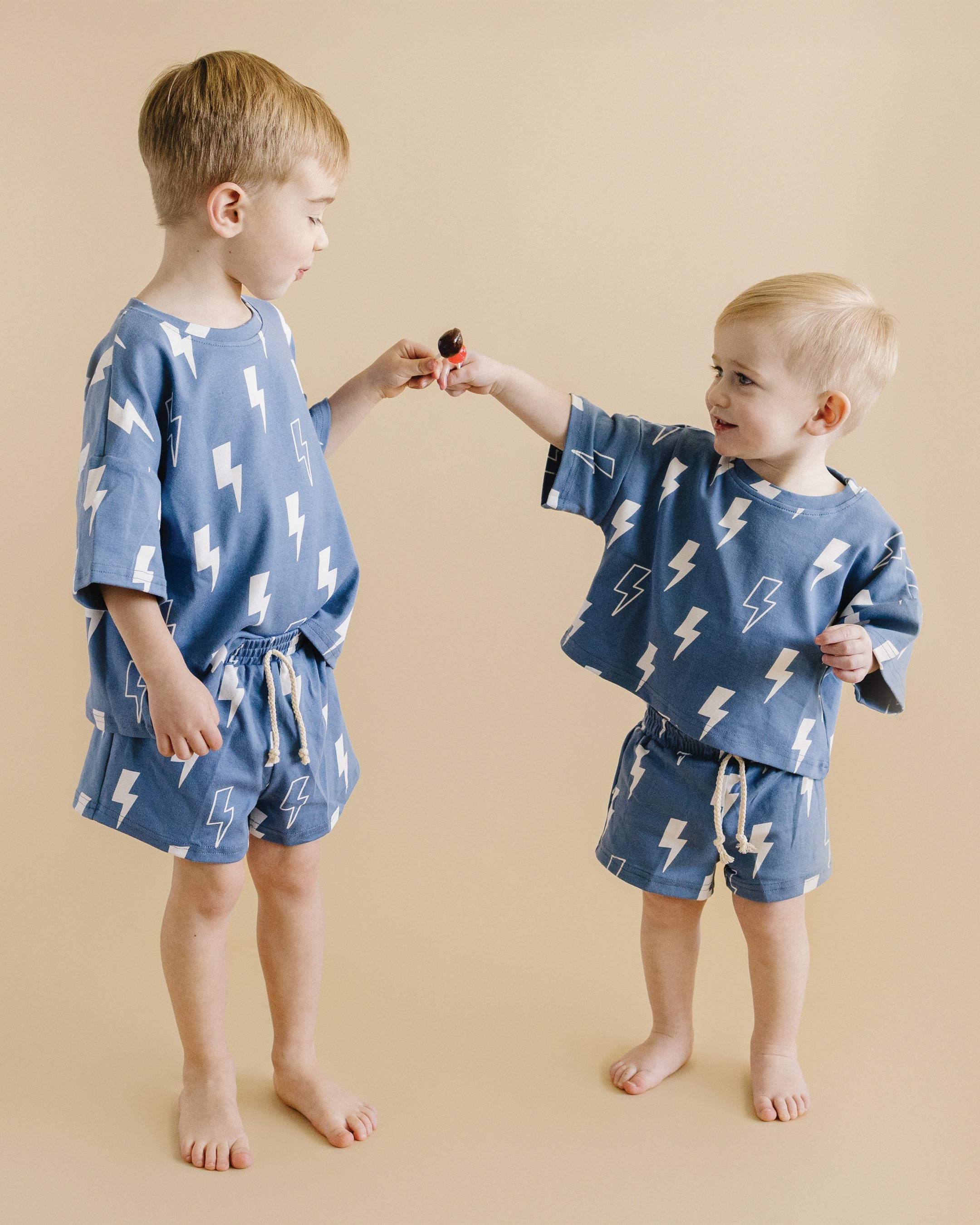 Two children wearing blue bolt print shorts set, enjoying a playful moment together in soft cotton outfits.