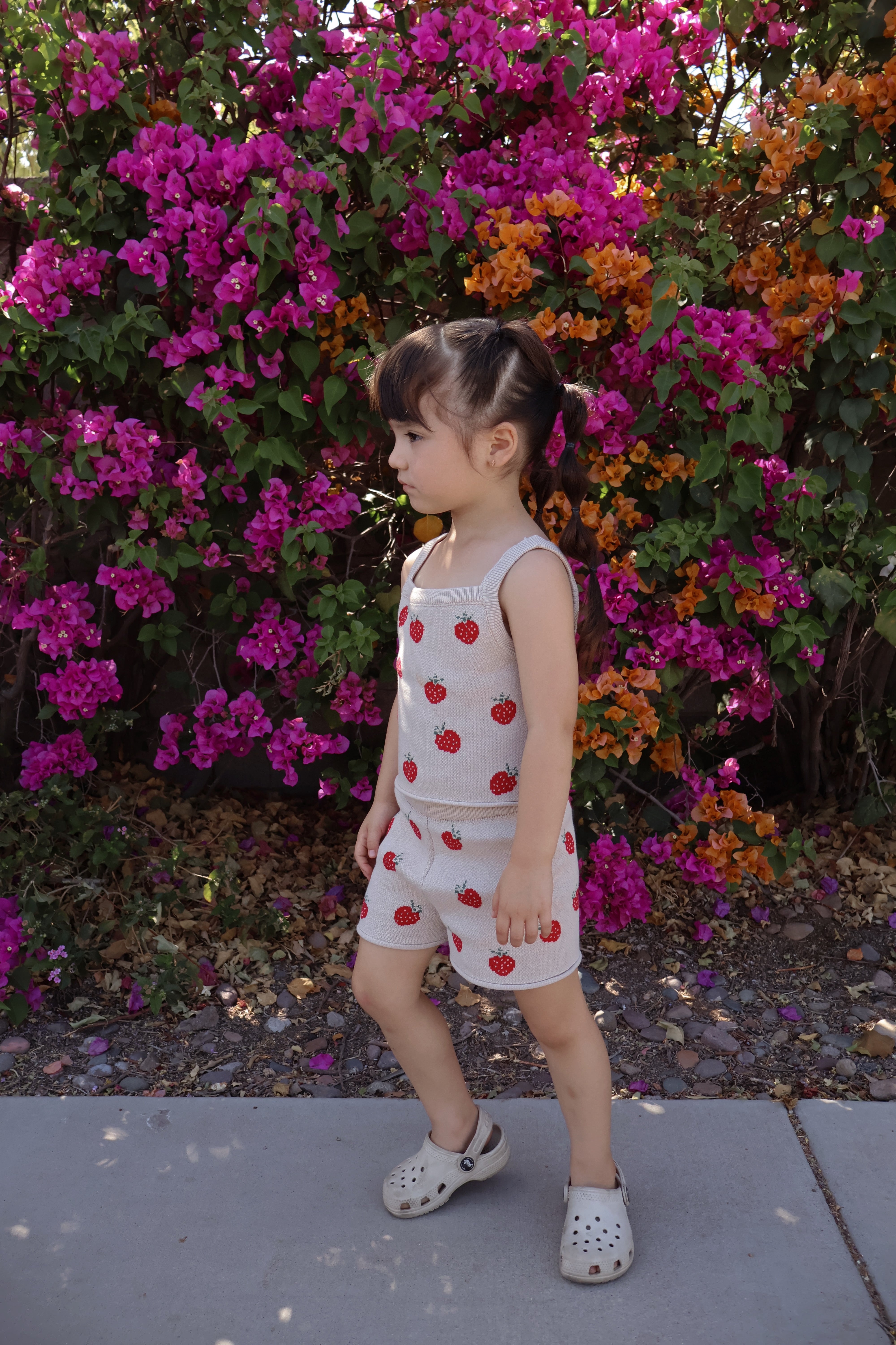 Little girl wearing a strawberry knit two-piece set against vibrant flower background.