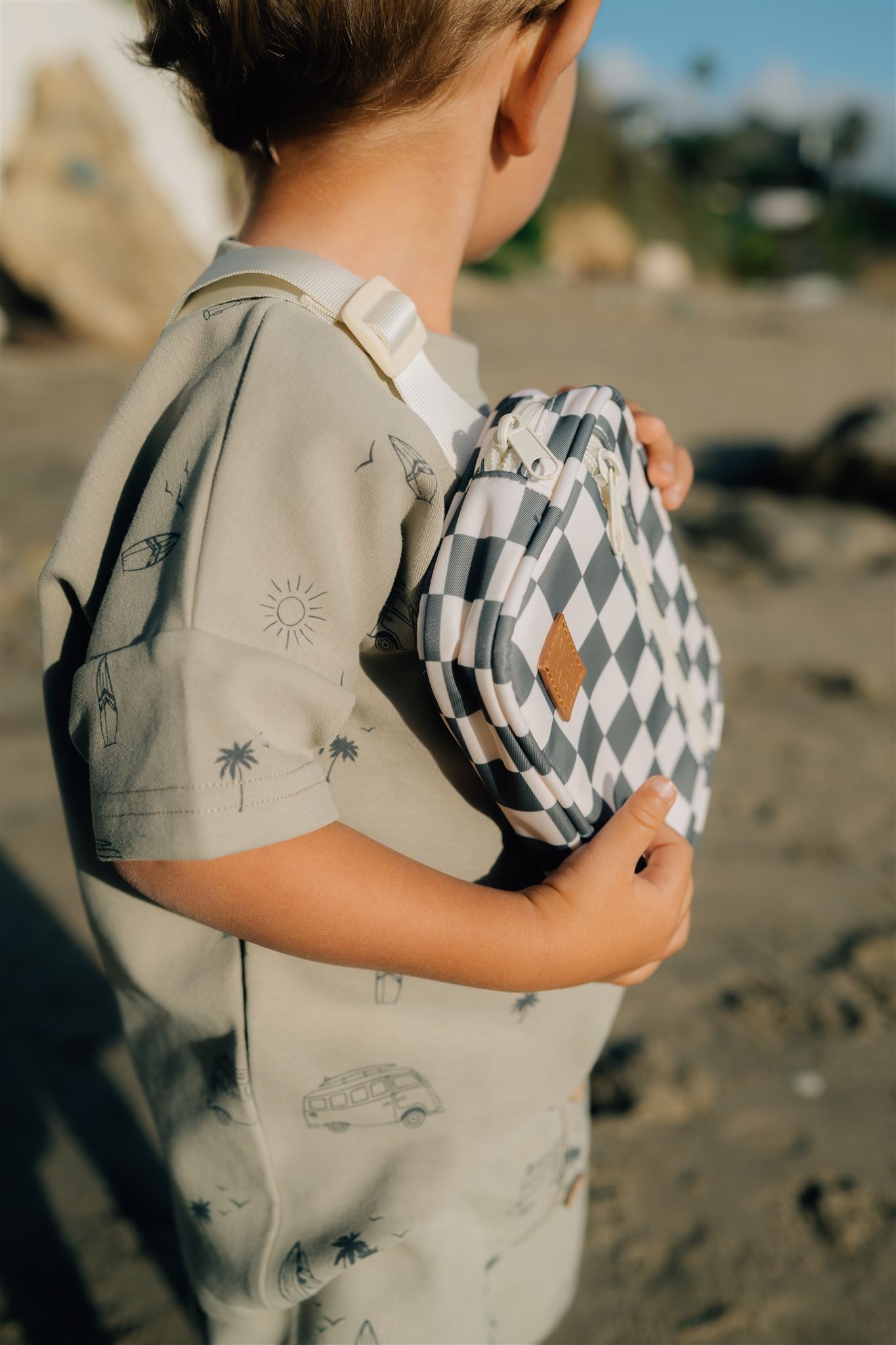 Child on the beach holding a mini fanny pack with a stylish checkered design.