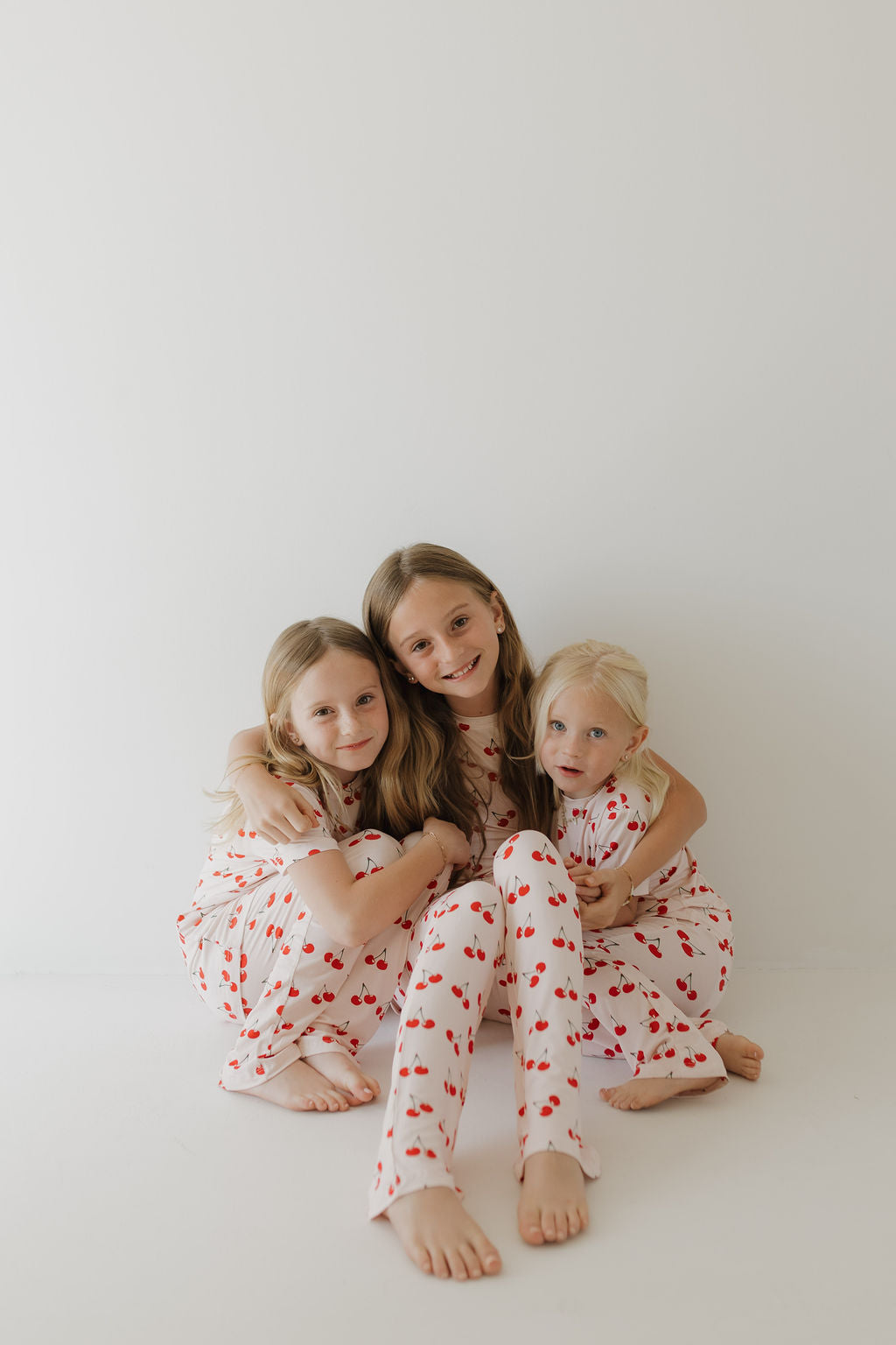 Three children in matching Cherry Orchard bamboo lounge sets, smiling and cozy on a light background.