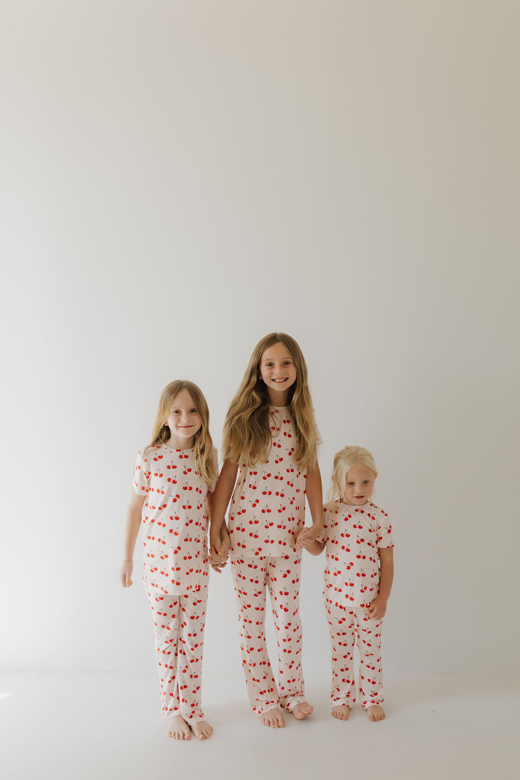 Three children wearing Cherry Orchard bamboo lounge sets with red cherry prints, smiling together against a neutral background.