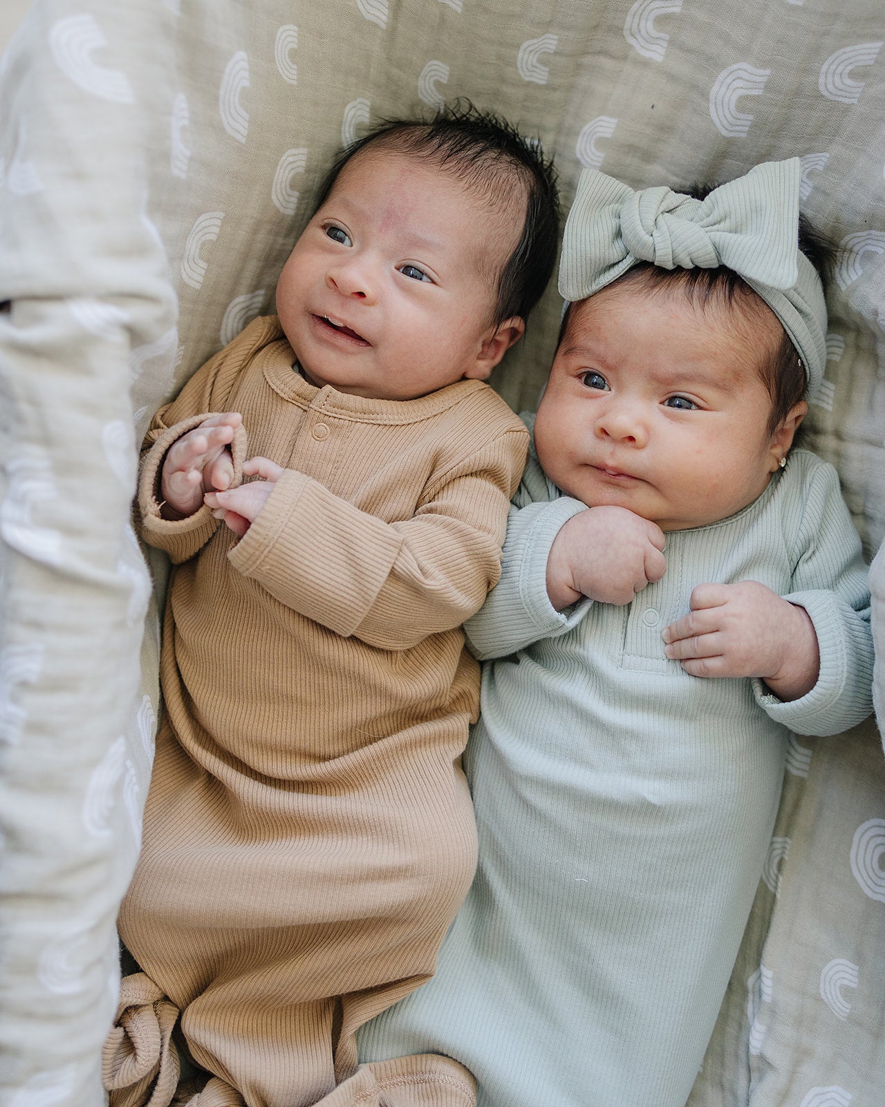 Two newborns in ribbed cotton gowns, one in café color and the other in soft green, showcasing cozy organic baby wear.