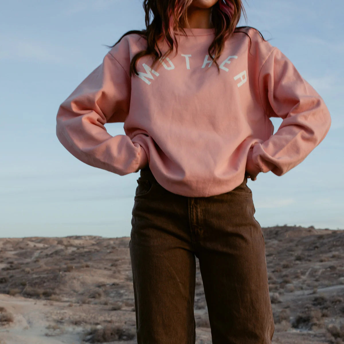 Womens coral sweatshirt with 'MOTHER' lettering, relaxed fit, styled outdoors against a scenic background.