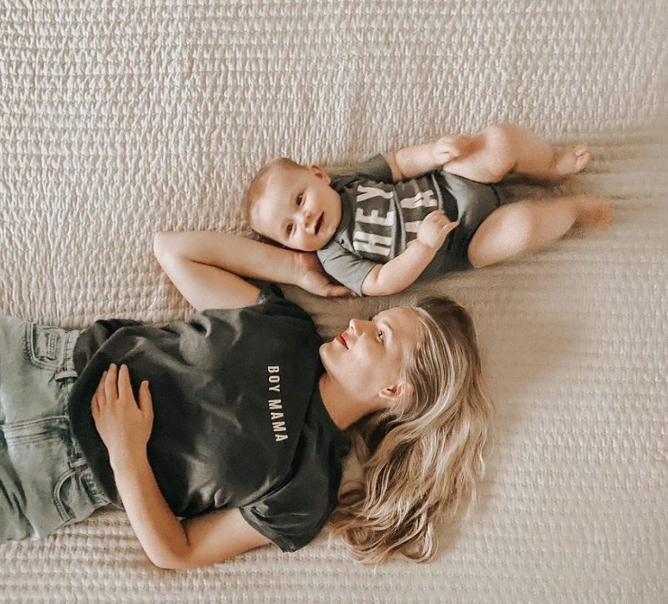 Mama and baby wearing matching graphic tees, relaxed and smiling on a soft blanket, embodying casual mom style.