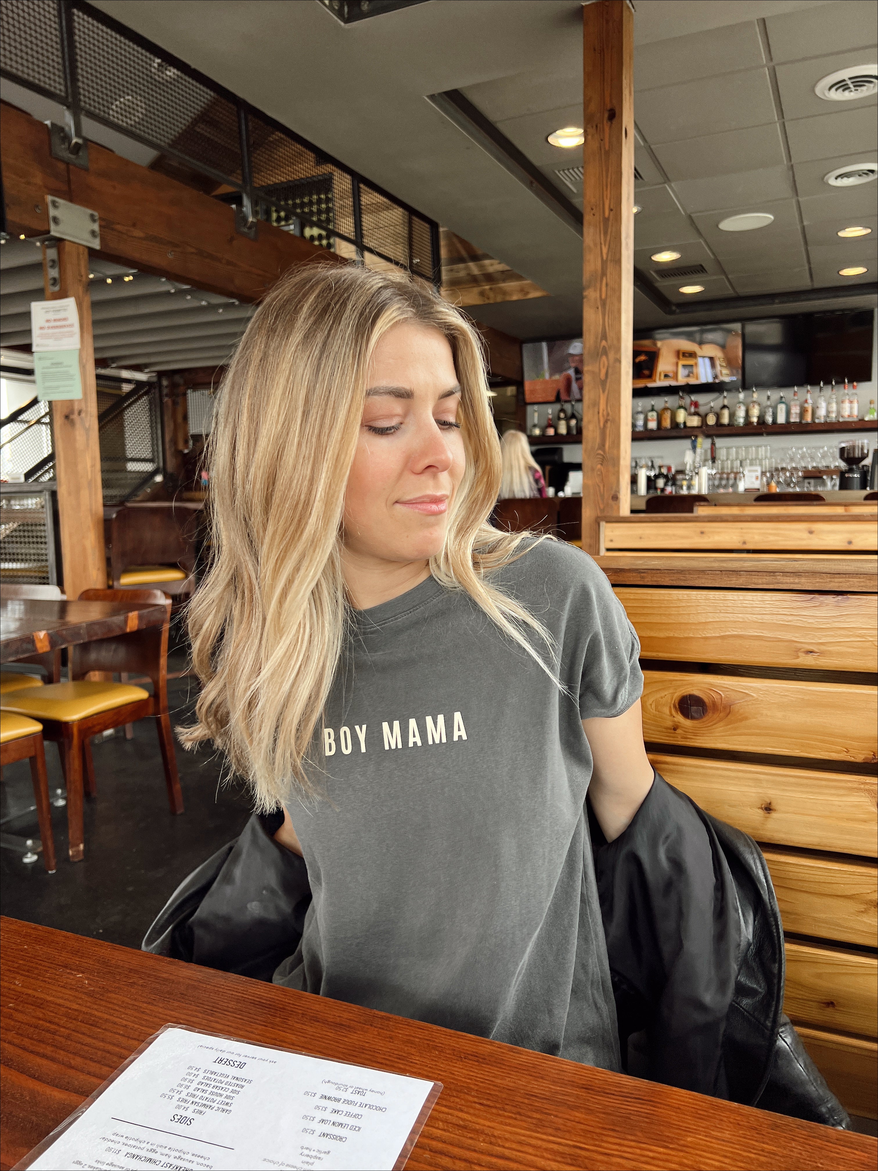 Woman wearing a gray 'Boy Mama' tee in a cafe, showcasing casual mom style and comfort.